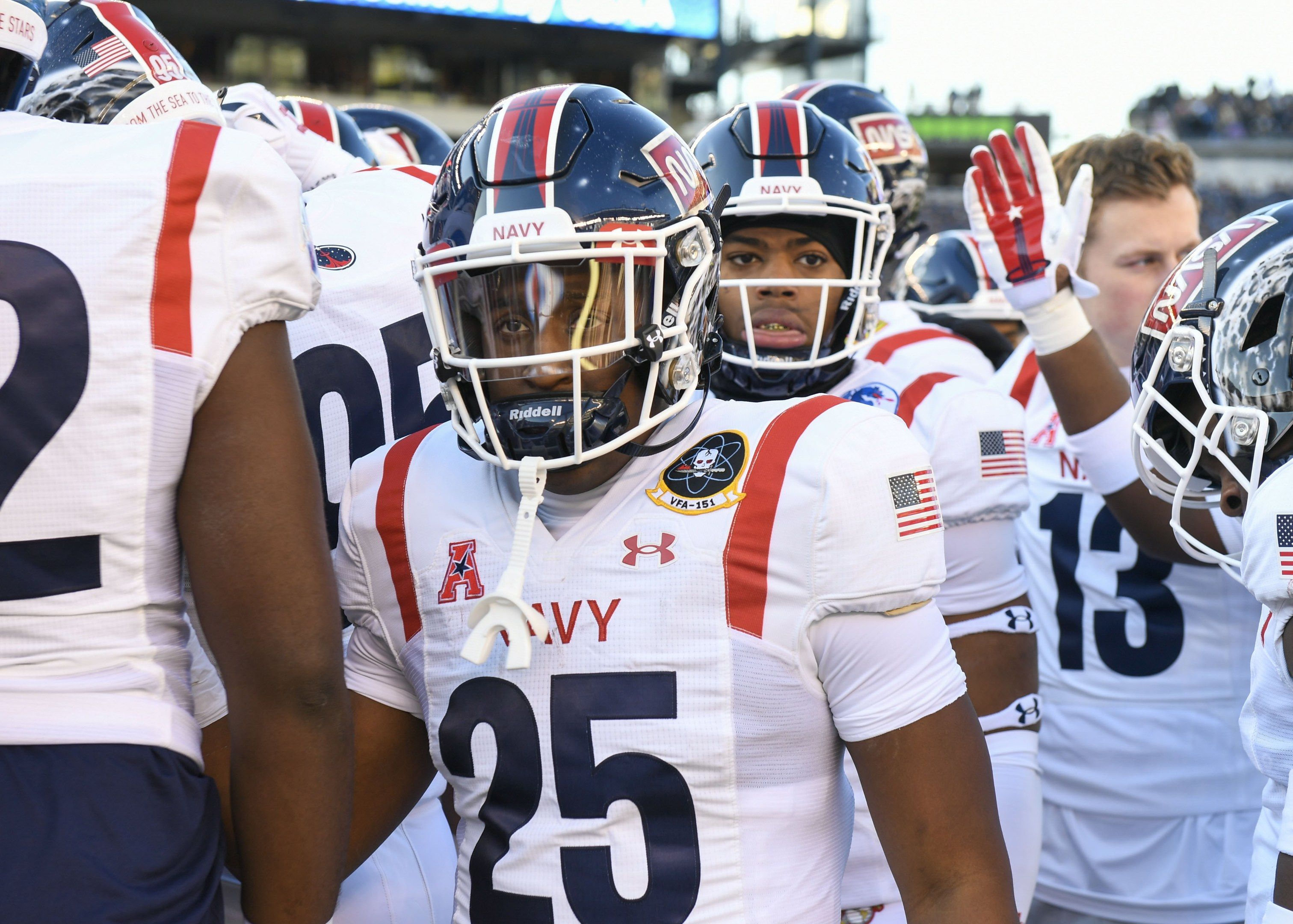 The image shows a group of men standing next to each other on a field, wearing helmets and gloves....
