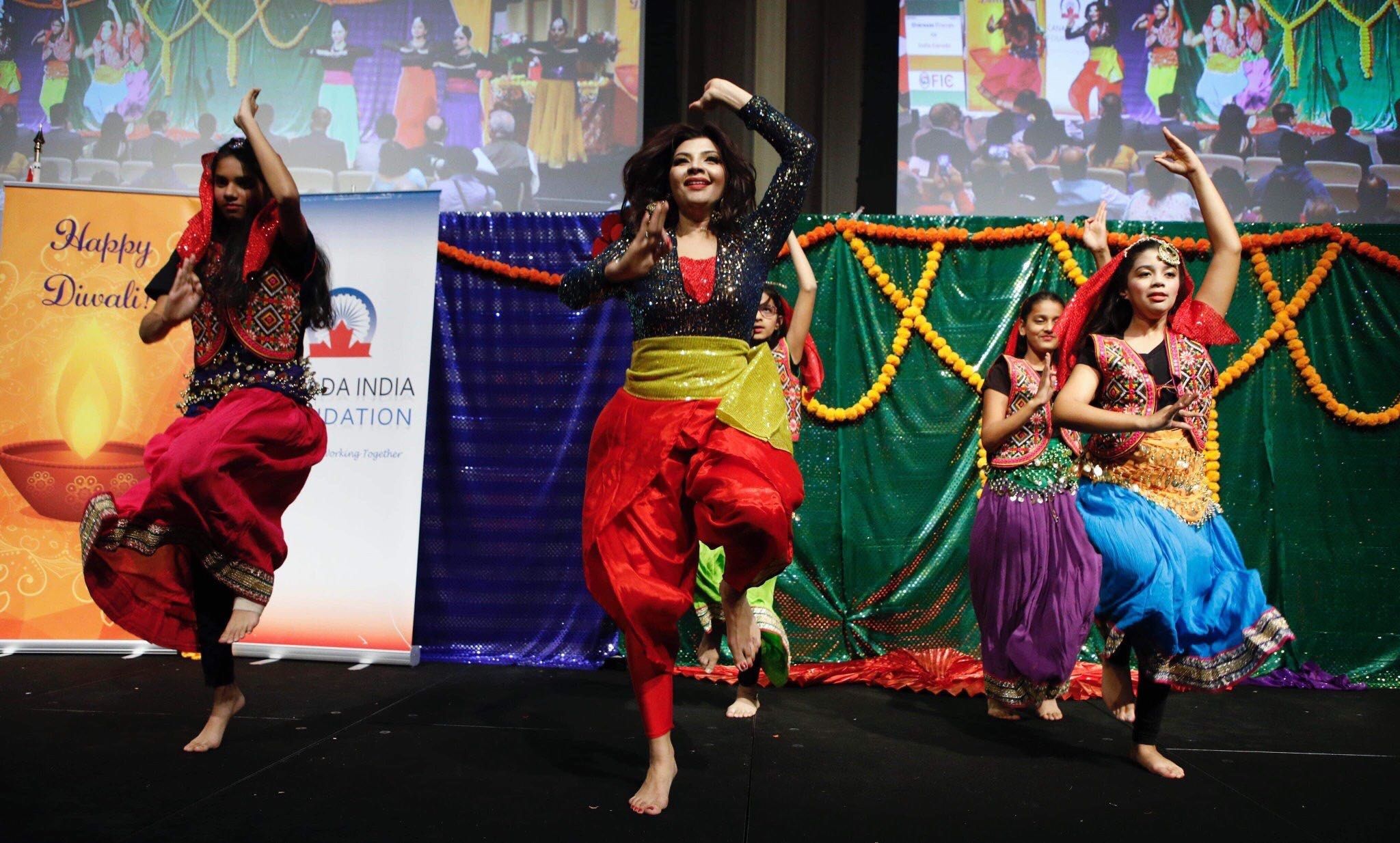 The image shows a group of young girls performing a traditional dance on a stage, surrounded by...