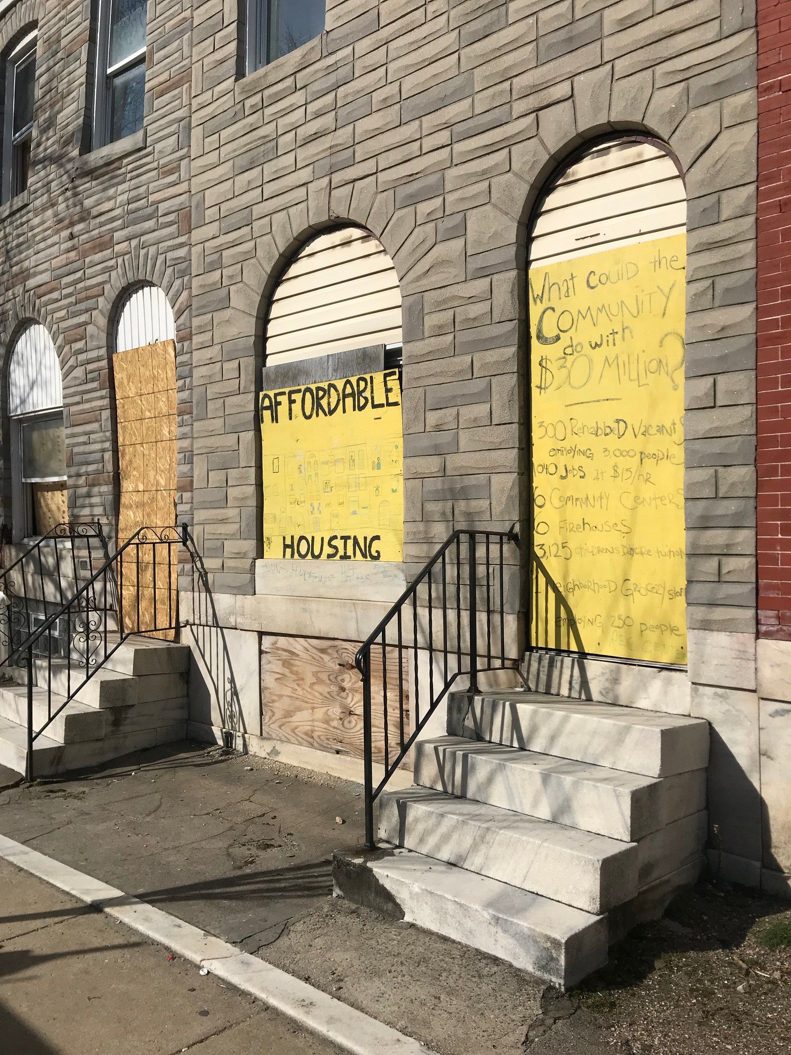 The image shows a building with boarded up windows and a sign on the side of it that reads...