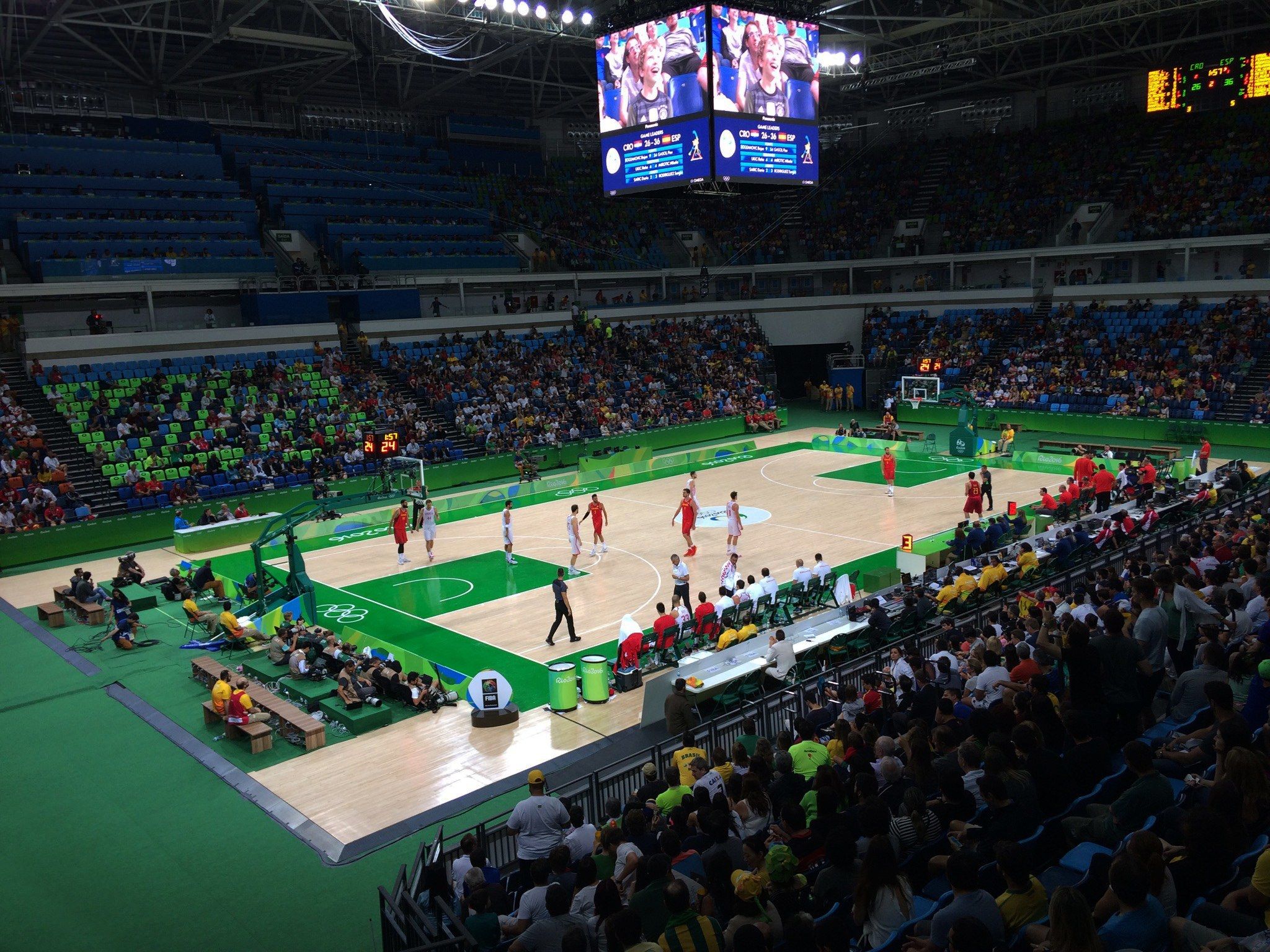 The image shows a large arena filled with lots of people watching a basketball game. There are...