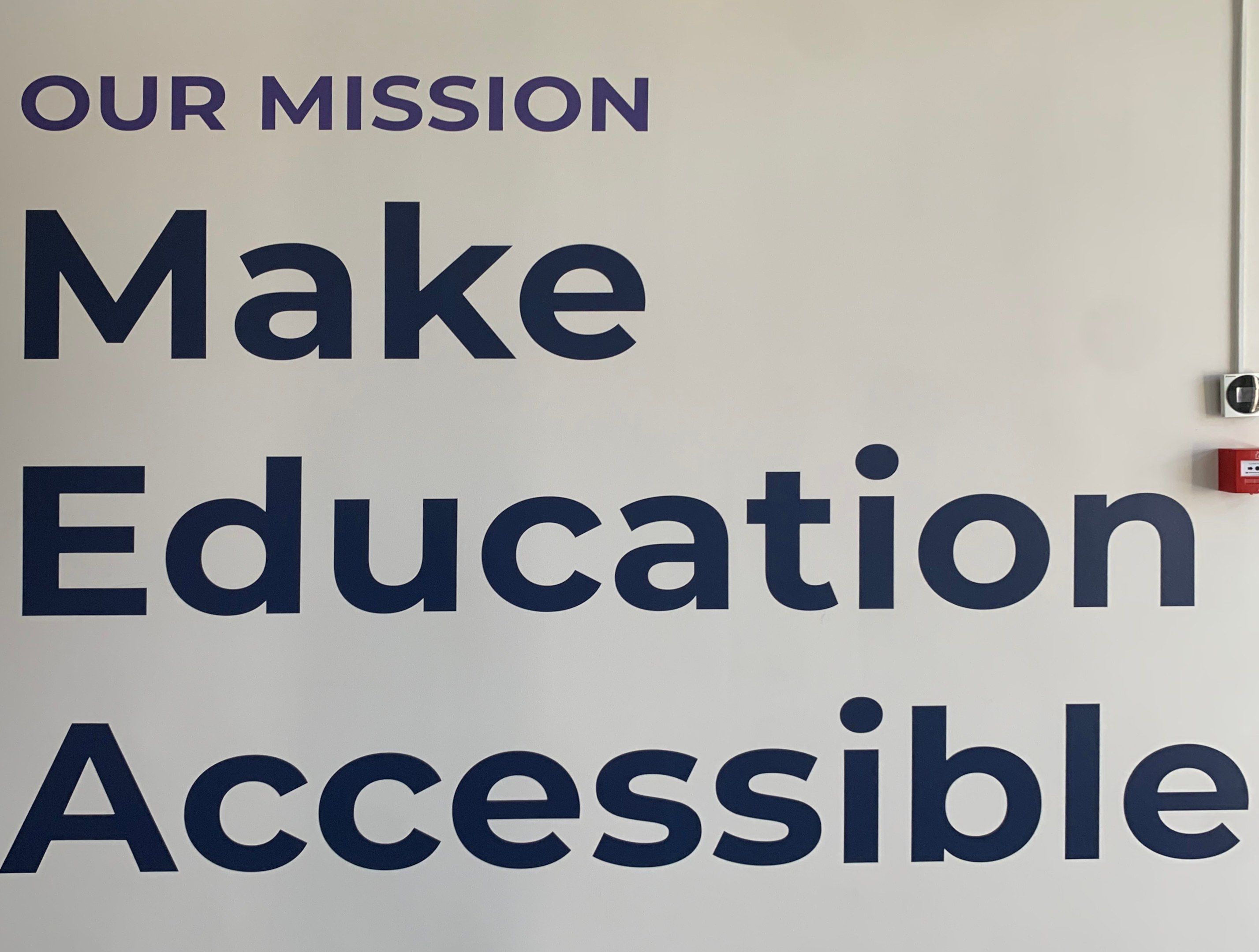The image shows a whiteboard with the words "Our Mission Make Education Accessible" written on it,...