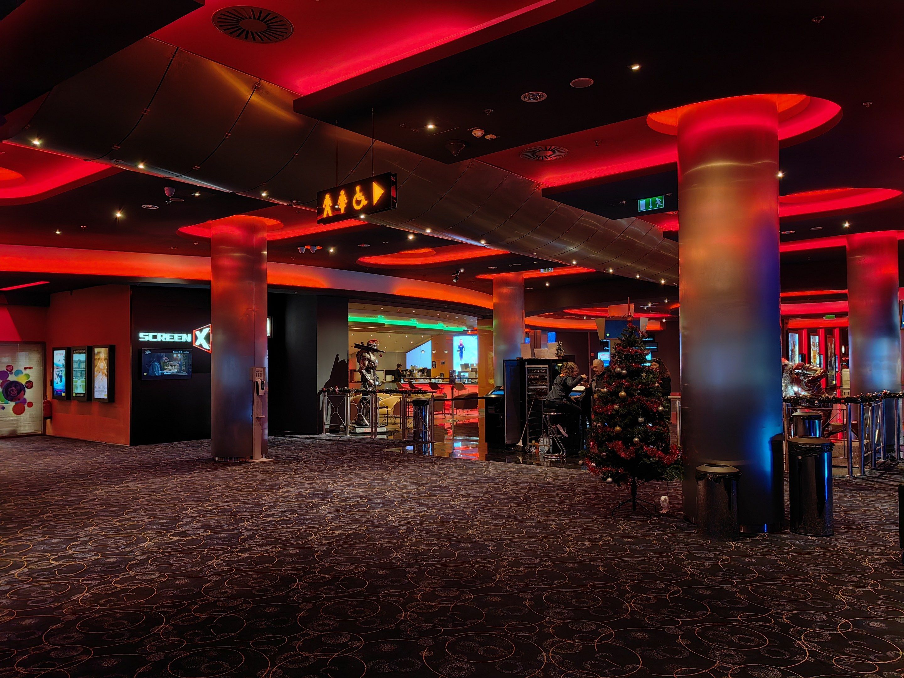 The image shows a large room with a Christmas tree in the middle of it, surrounded by pillars and...