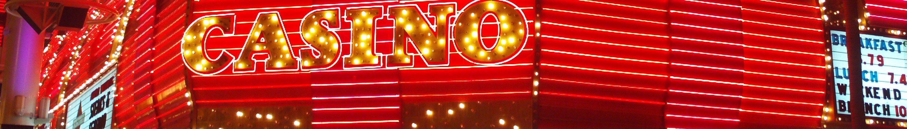 The image shows a casino sign lit up at night in front of a building, with text on the wall and...