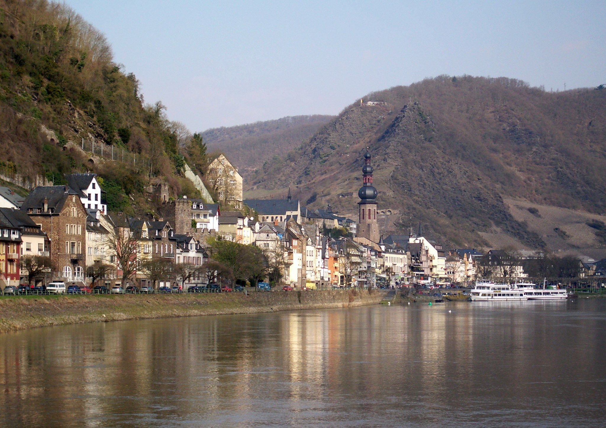 The image shows a picturesque view of a small town on the banks of a river, with boats on the...