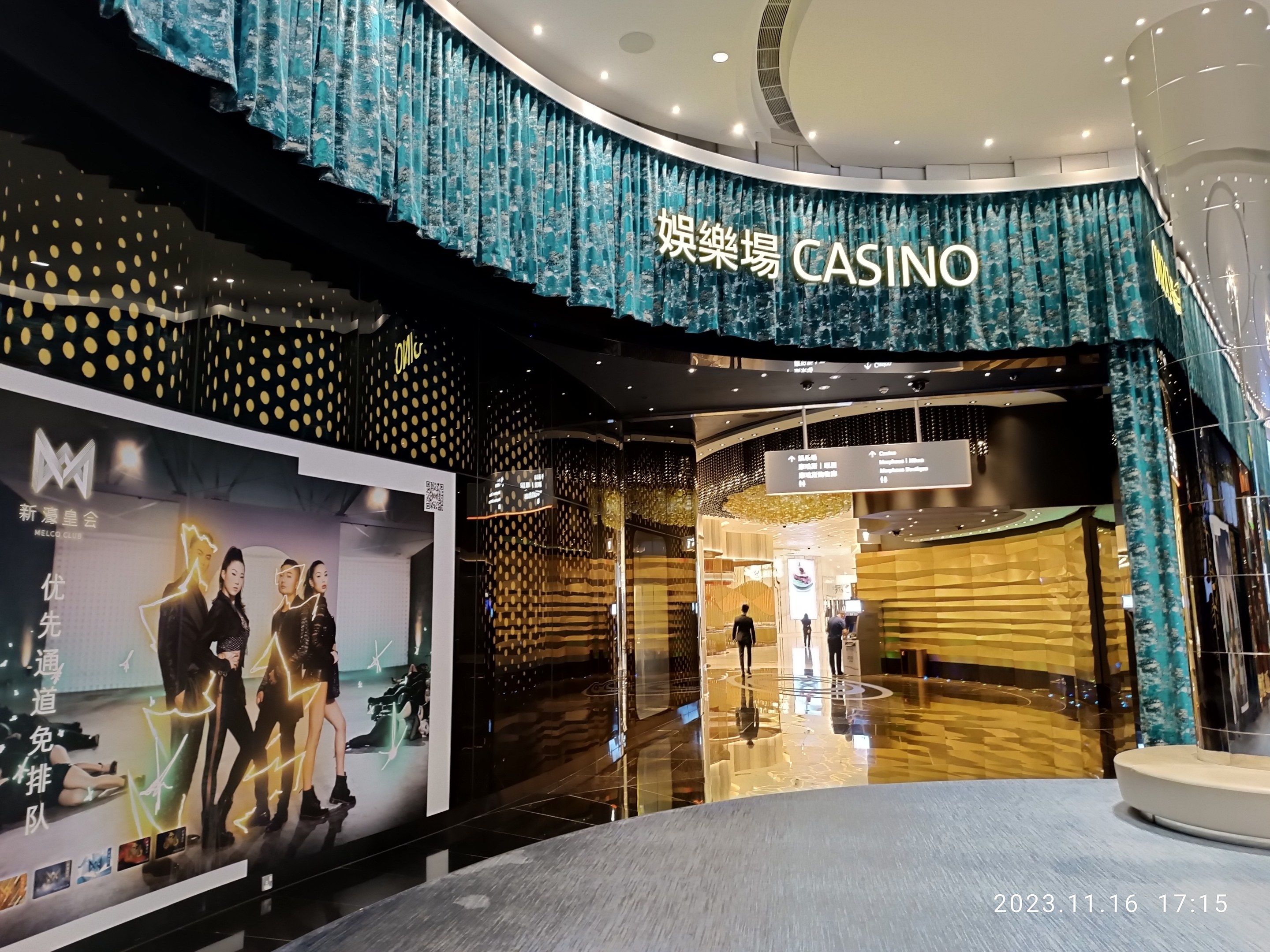 The image shows the entrance to a casino with a large screen on the wall, a banner with pictures...