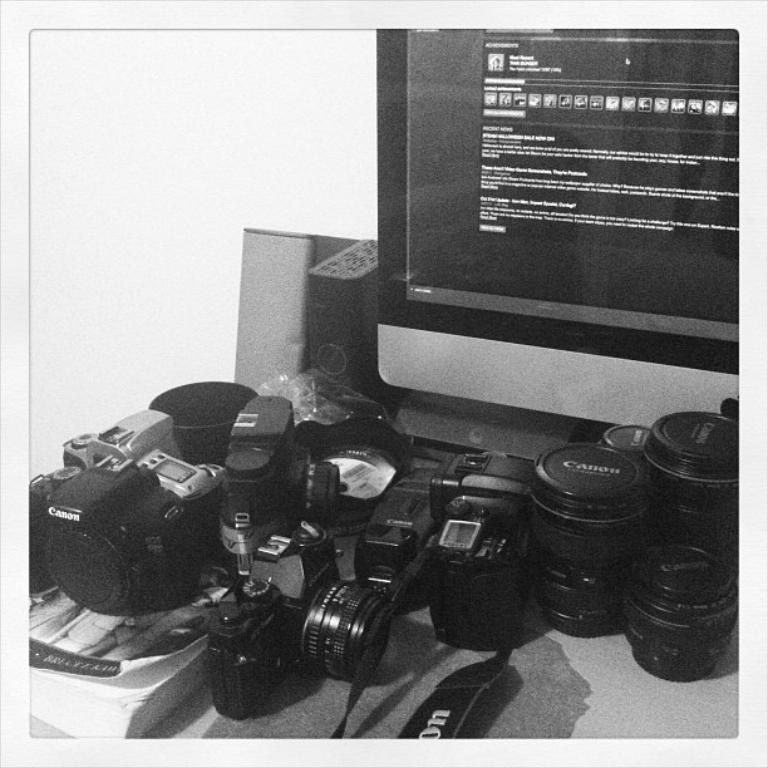 In this image there are few cameras, a computer, CPU and some other objects on the table.