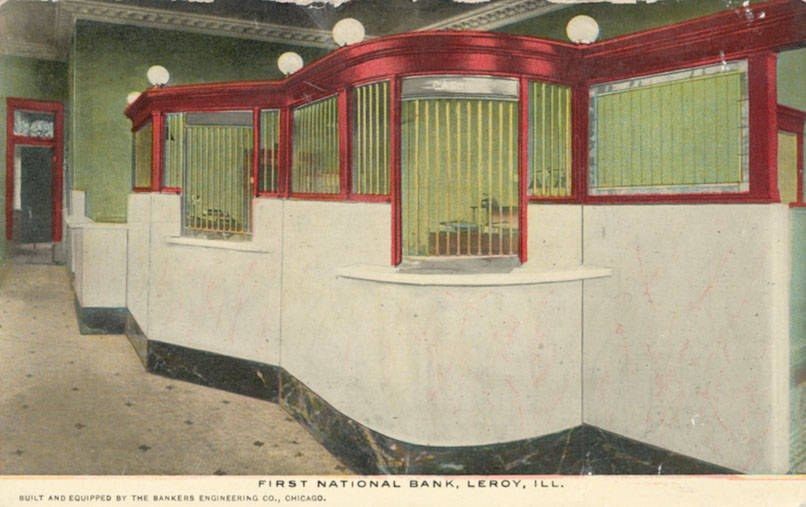 The image shows an old postcard of the first national bank in Leroy, Illinois. It features a room...
