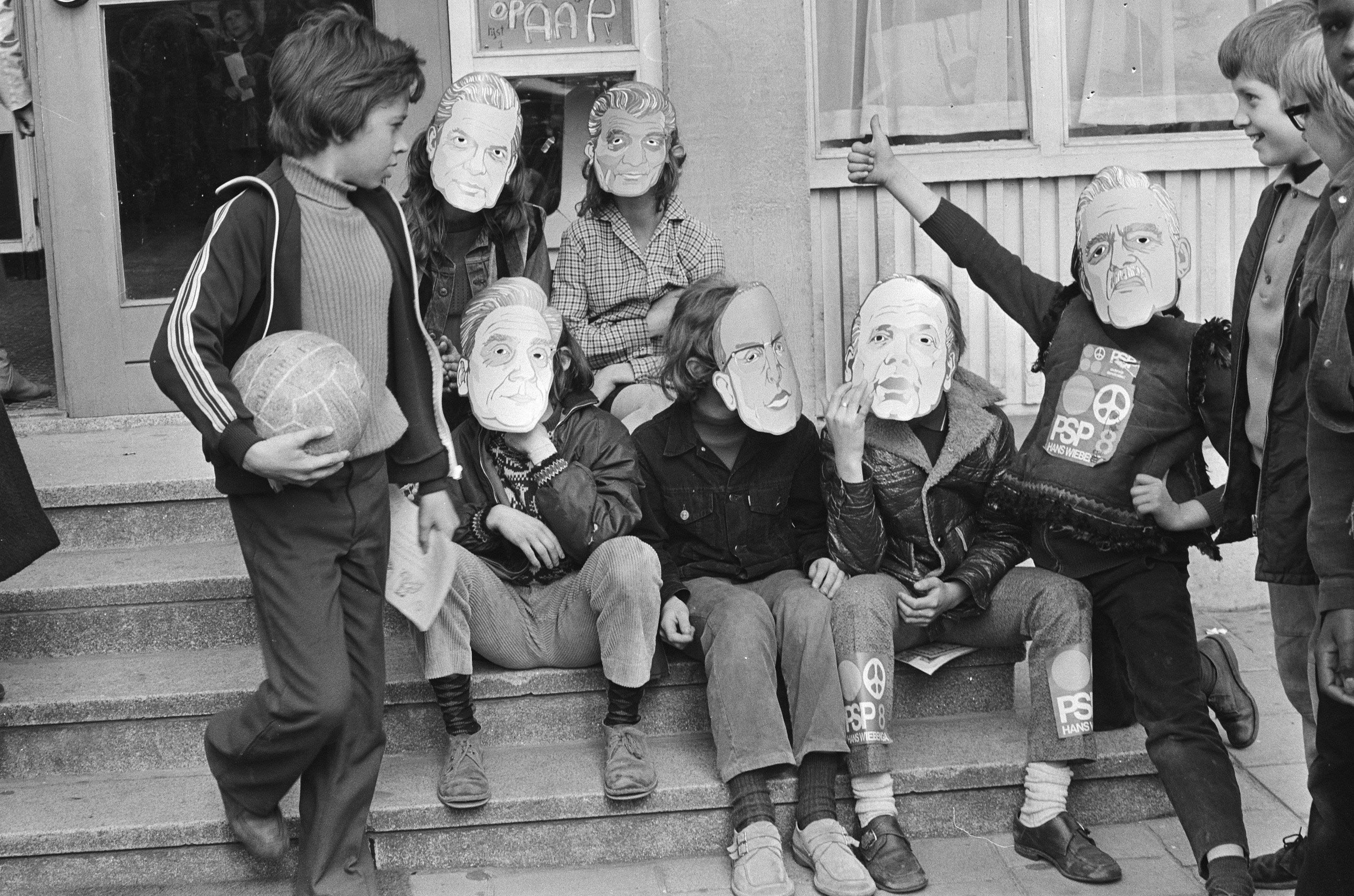 The image shows a group of children sitting on the steps of a building with masks on their faces....
