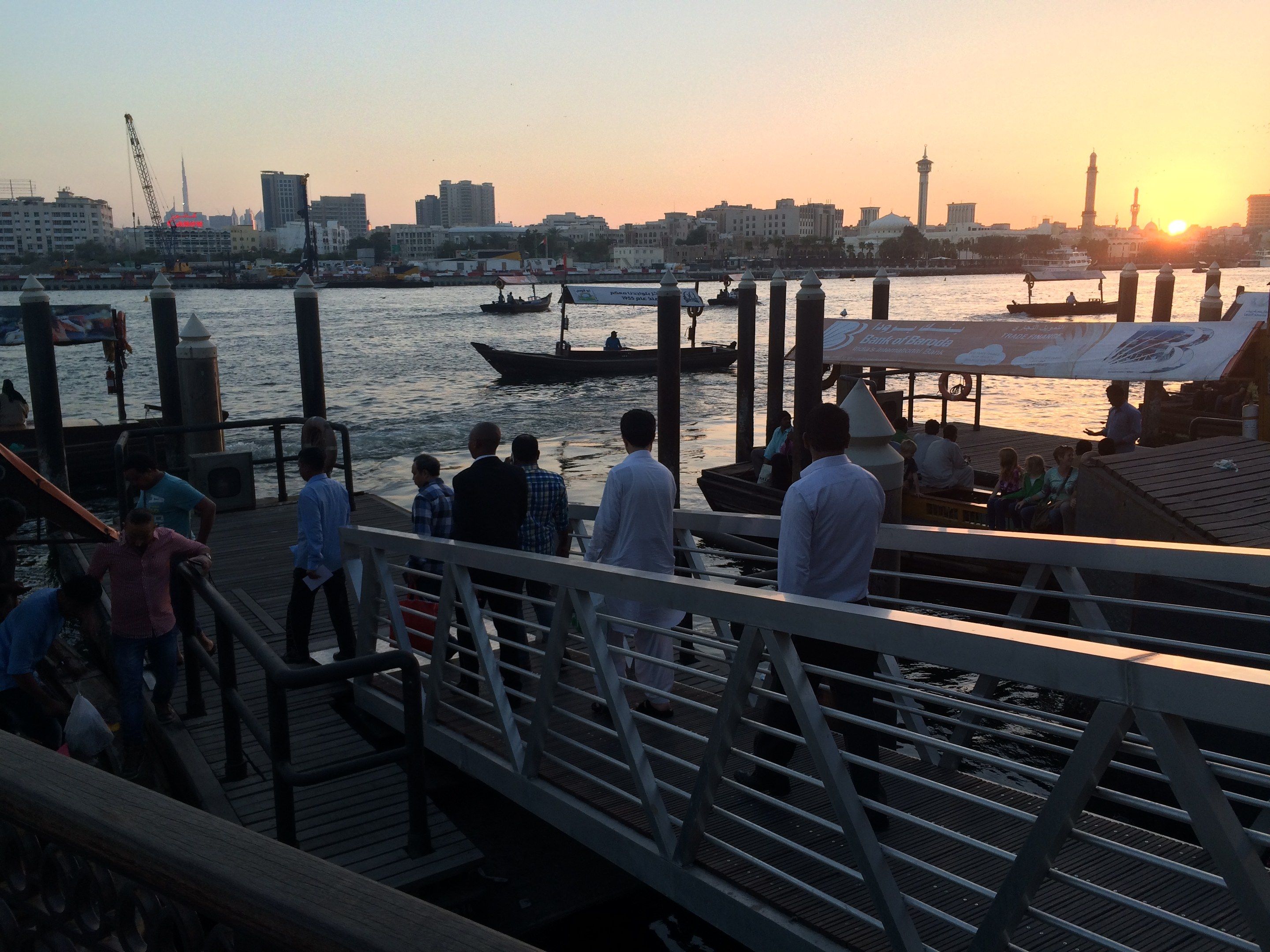 The image shows a group of people standing on top of a pier next to a body of water, with boats in...