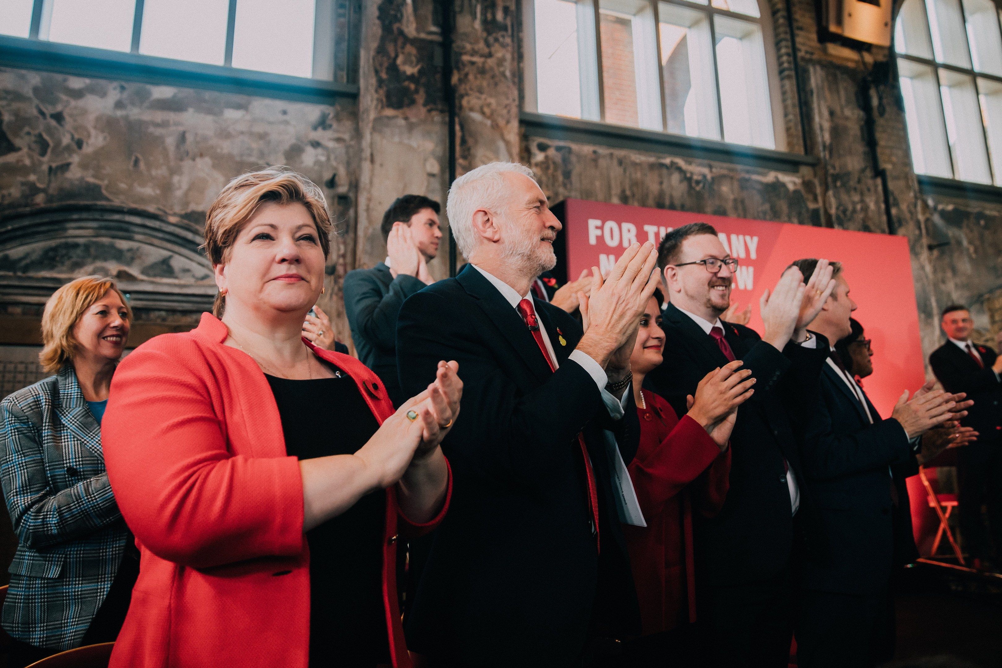 The image shows a group of people standing in front of a crowd, clapping their hands in...