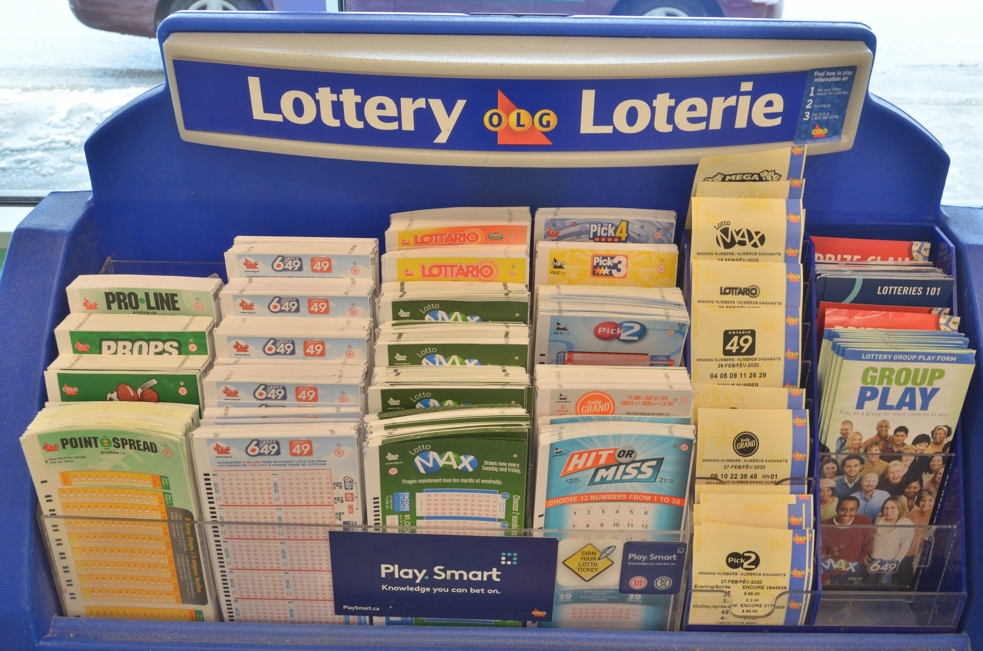 The image shows a blue display case filled with lots of lottery tickets in front of a glass window,...