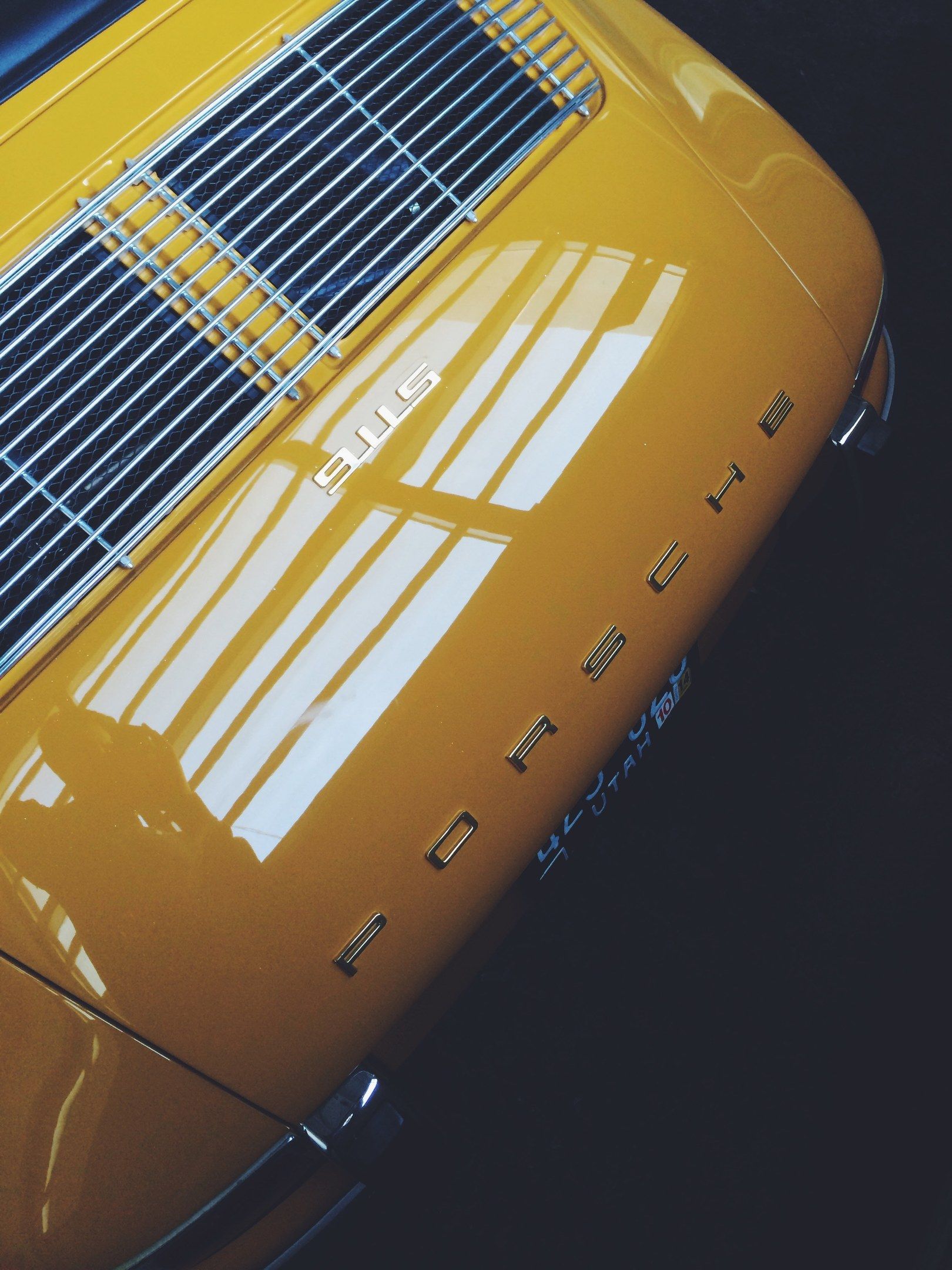 The image shows a close up of a yellow Porsche 911 parked in a parking lot. The car is a bright...