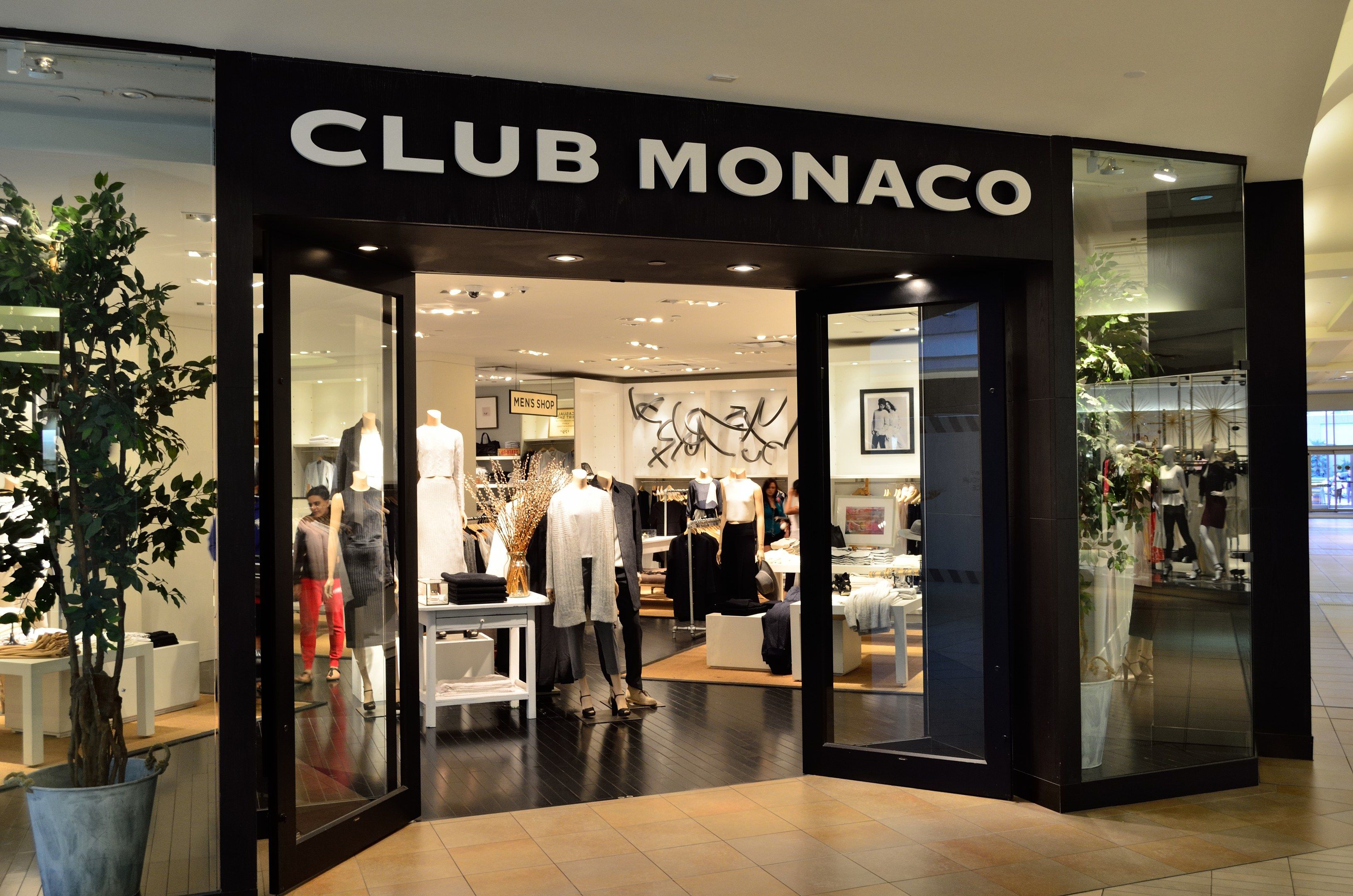 The image shows a Club Monaco store in a shopping mall, with glass walls and doors, mannequins...