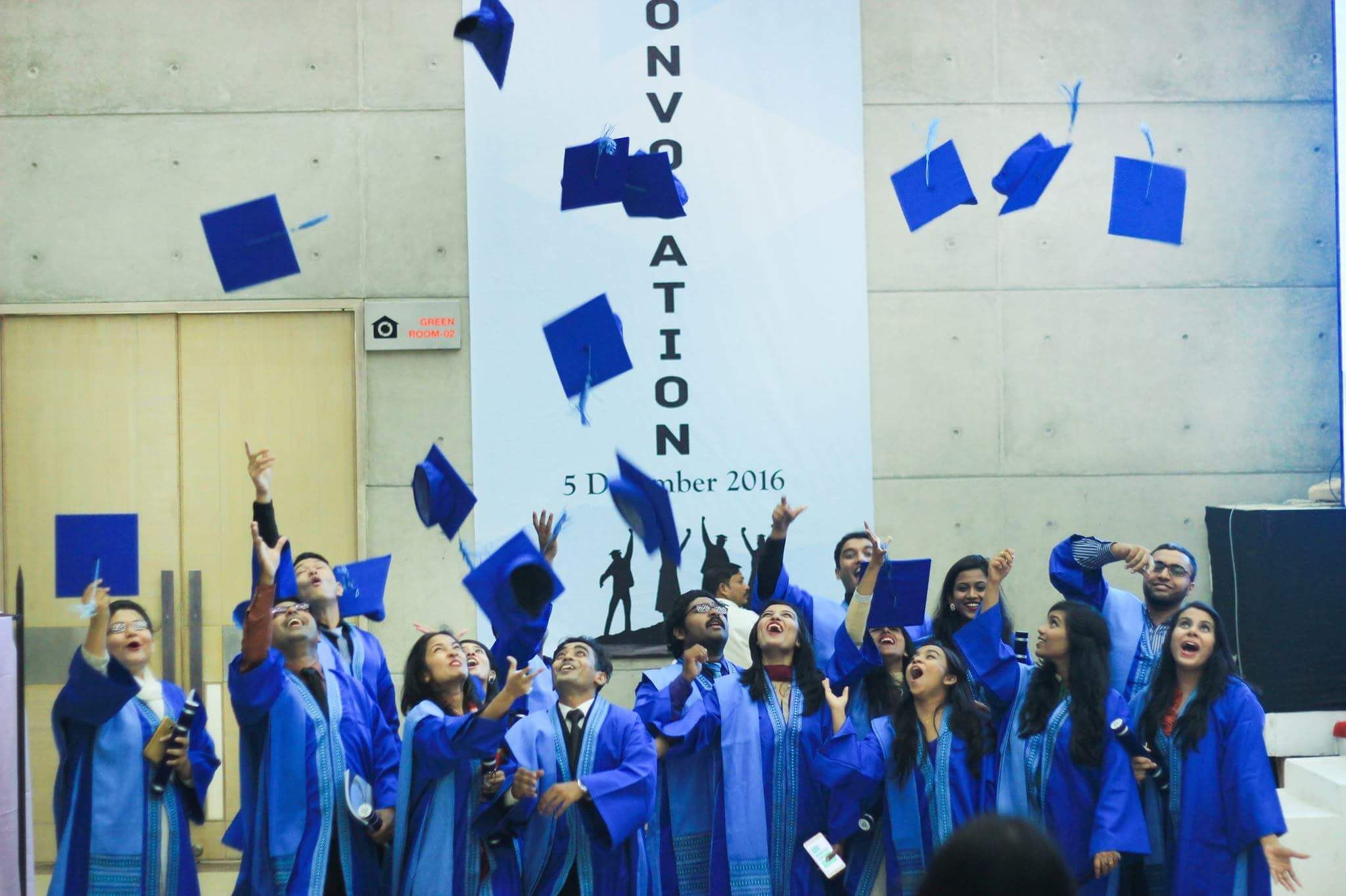 The image shows a group of people in blue graduation robes and hats throwing their hats in the air...