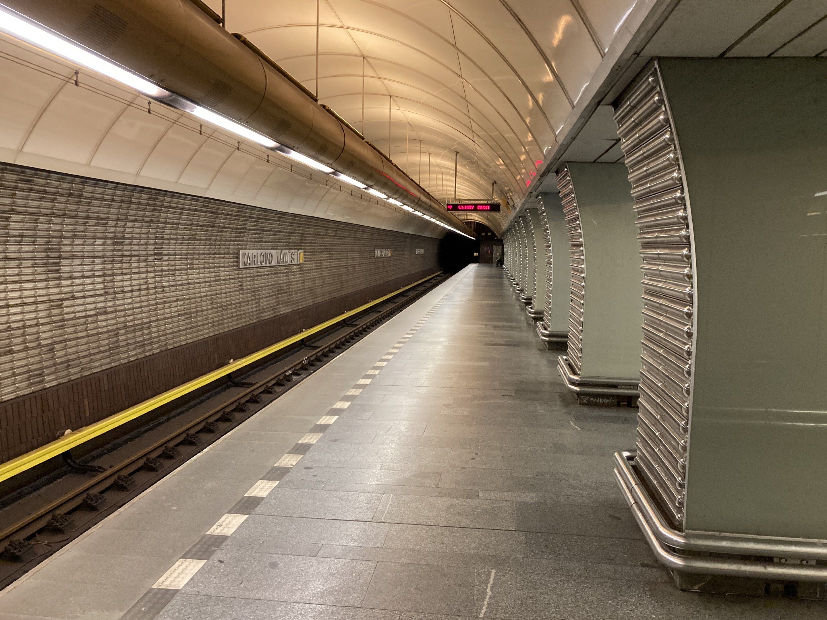 The image shows a subway station with a train on the tracks, illuminated by lights attached to the...
