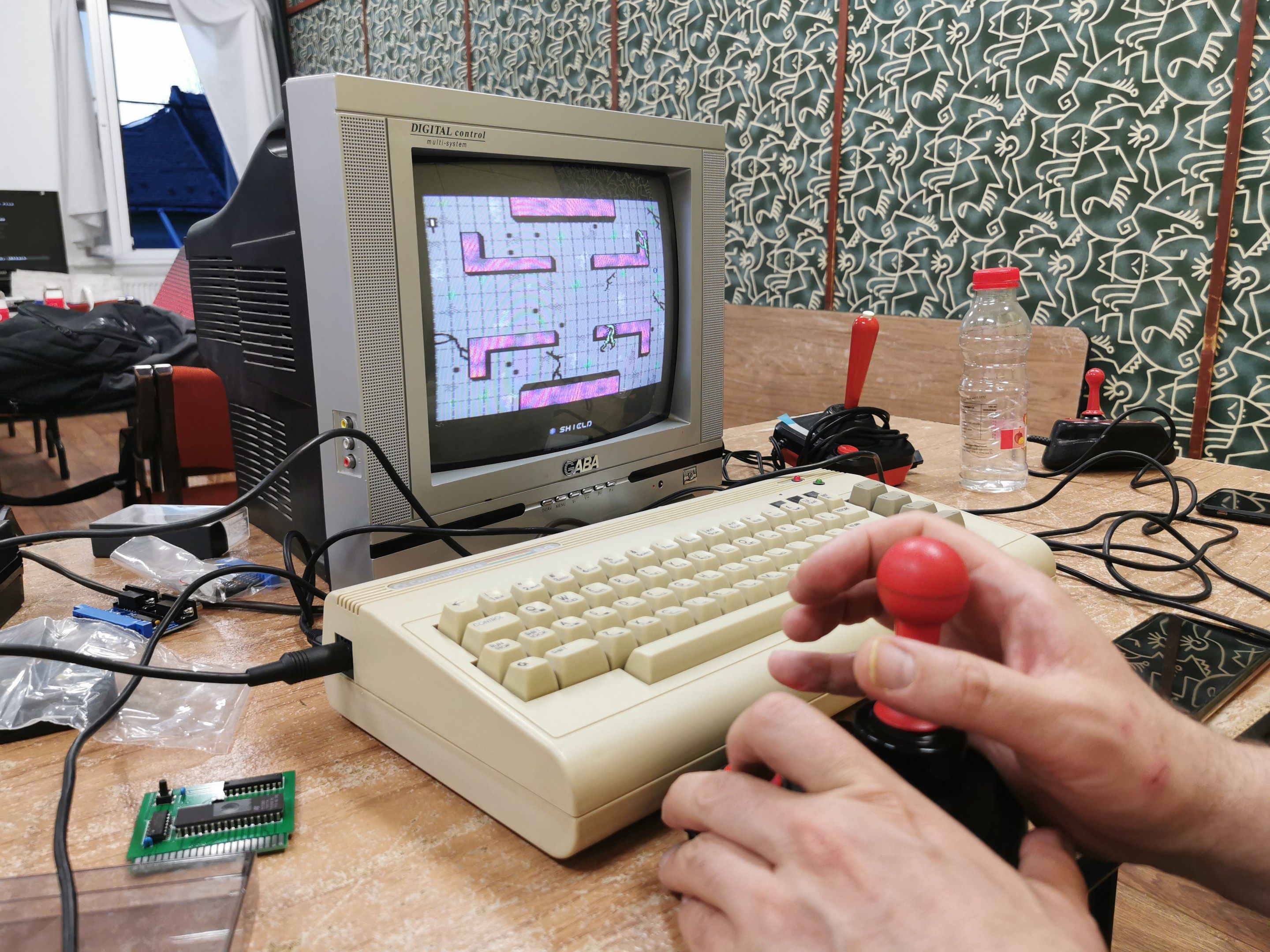 The image shows a person playing a video game on an old computer, with a joystick in their hand. On...