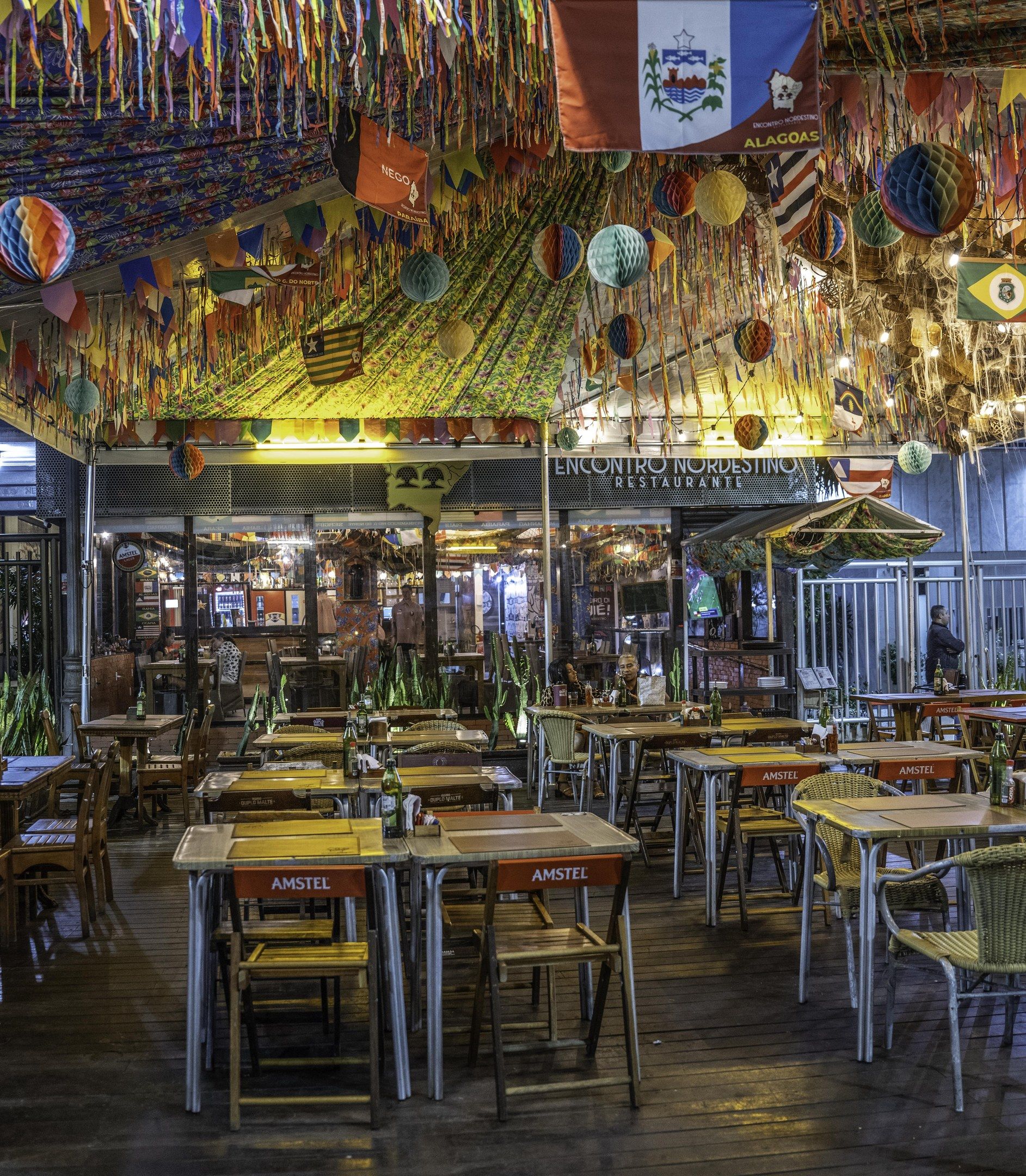 The image shows a restaurant with tables and chairs in the middle of it, surrounded by bottles and...