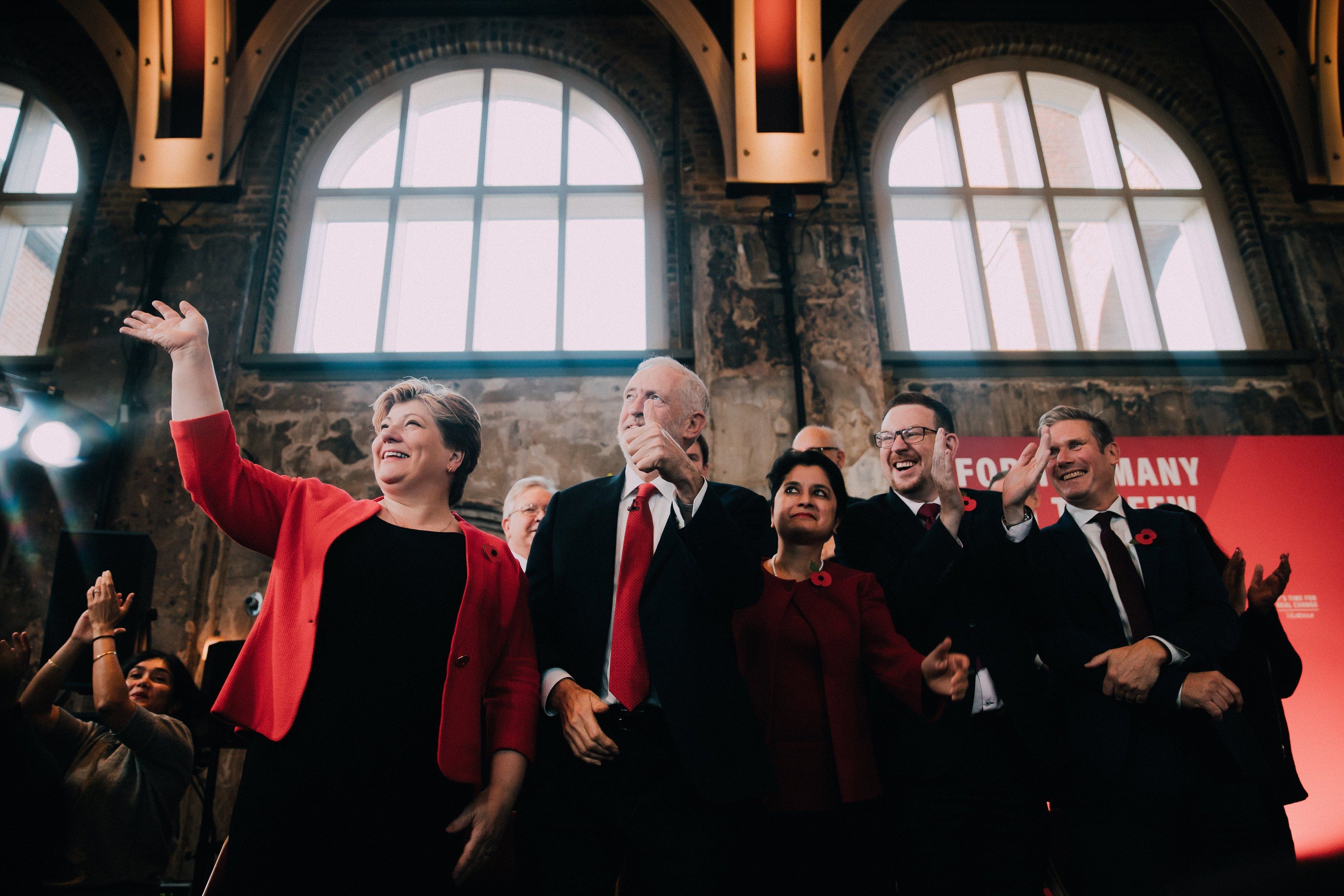 The image shows a group of people standing next to each other in front of a crowd, clapping their...