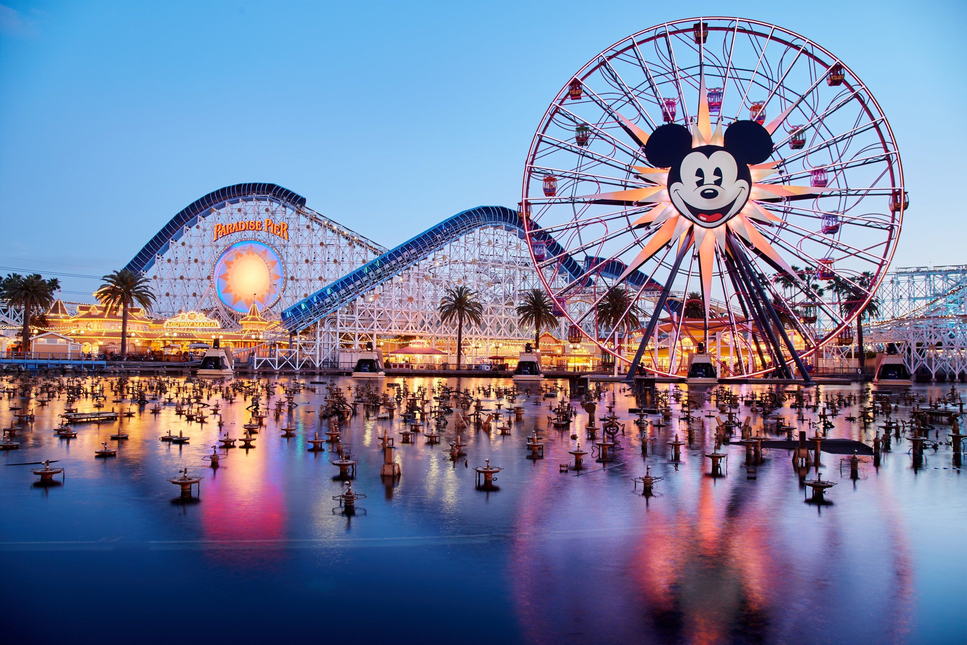 The image shows a vibrant scene of Disneyland's California Adventure at dusk, with a giant Mickey...