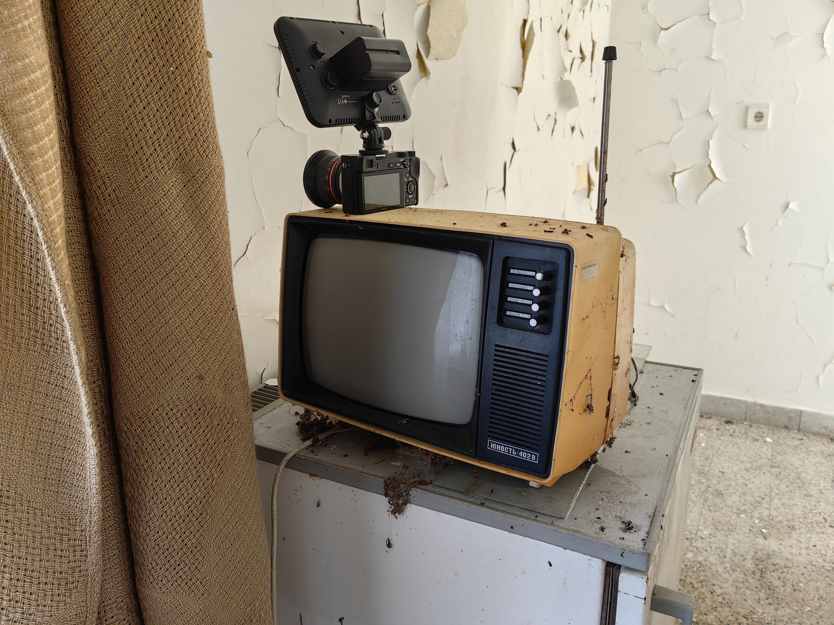The image shows an old television sitting on top of a table next to a camera, with a curtain on the...