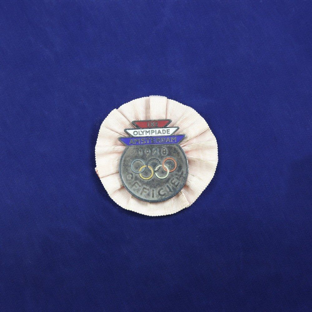 The image shows a blue cloth with a badge featuring the Olympic logo on it. The badge is in the...