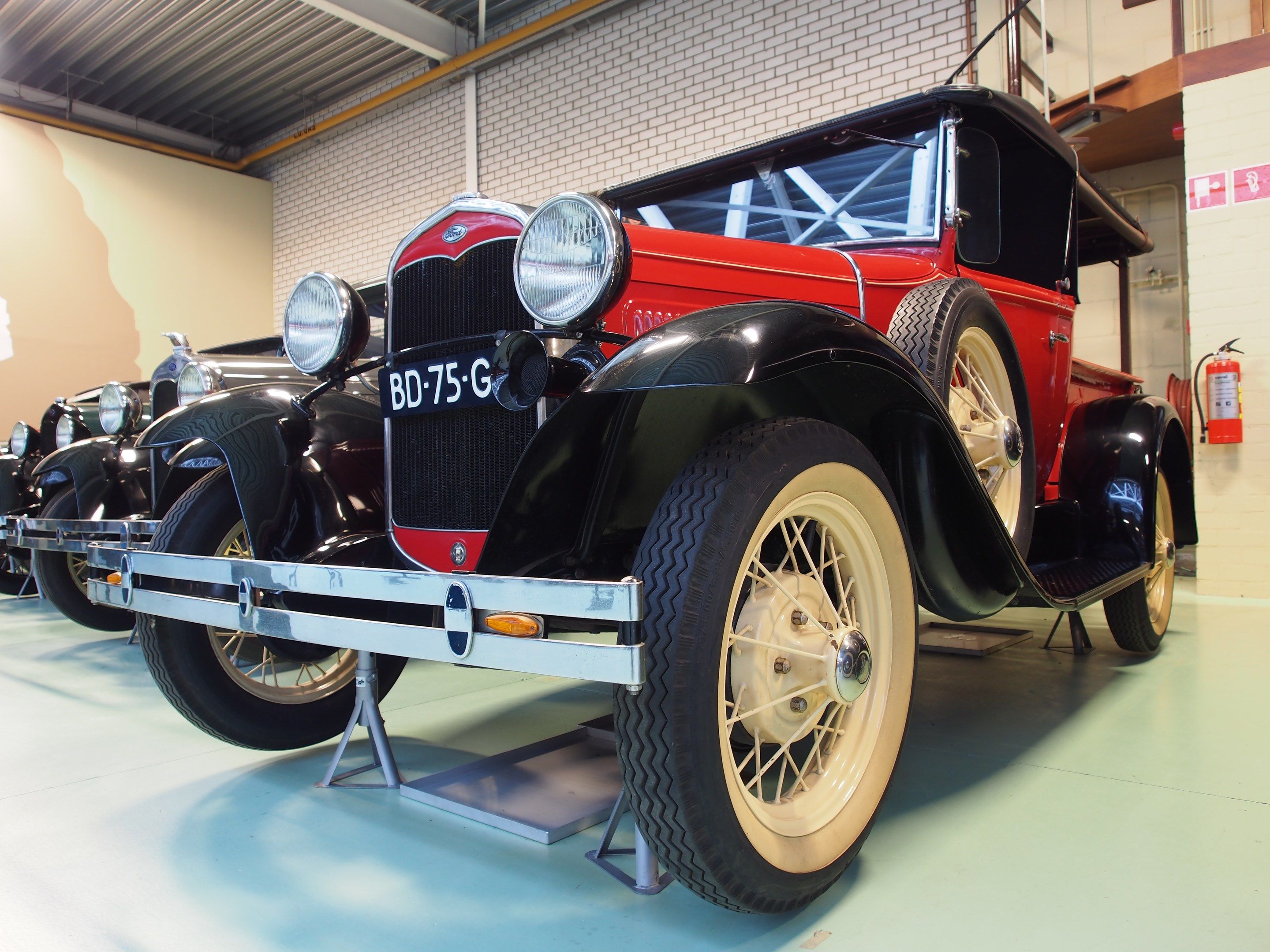 The image shows a row of vintage cars on display in a museum, with a wall in the background, a fire...