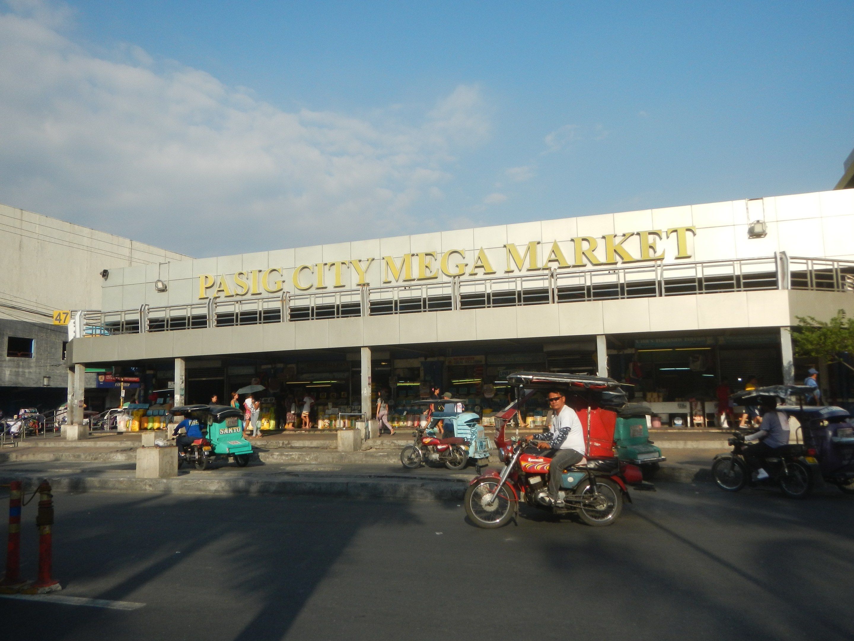 The image shows a bustling Pasig City Mega Market, with vehicles on the road and people walking...