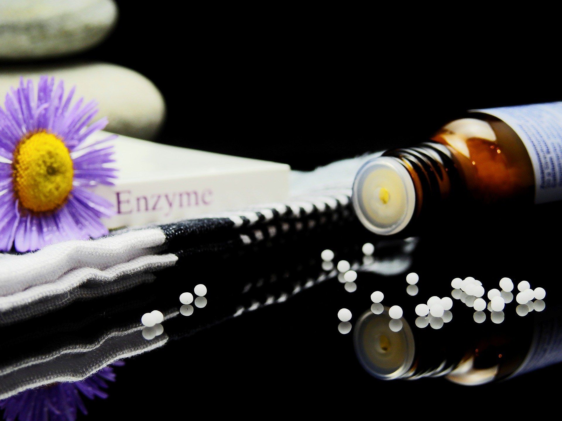 The image shows a bottle of enzyme essential oil sitting on top of a table next to a purple flower,...
