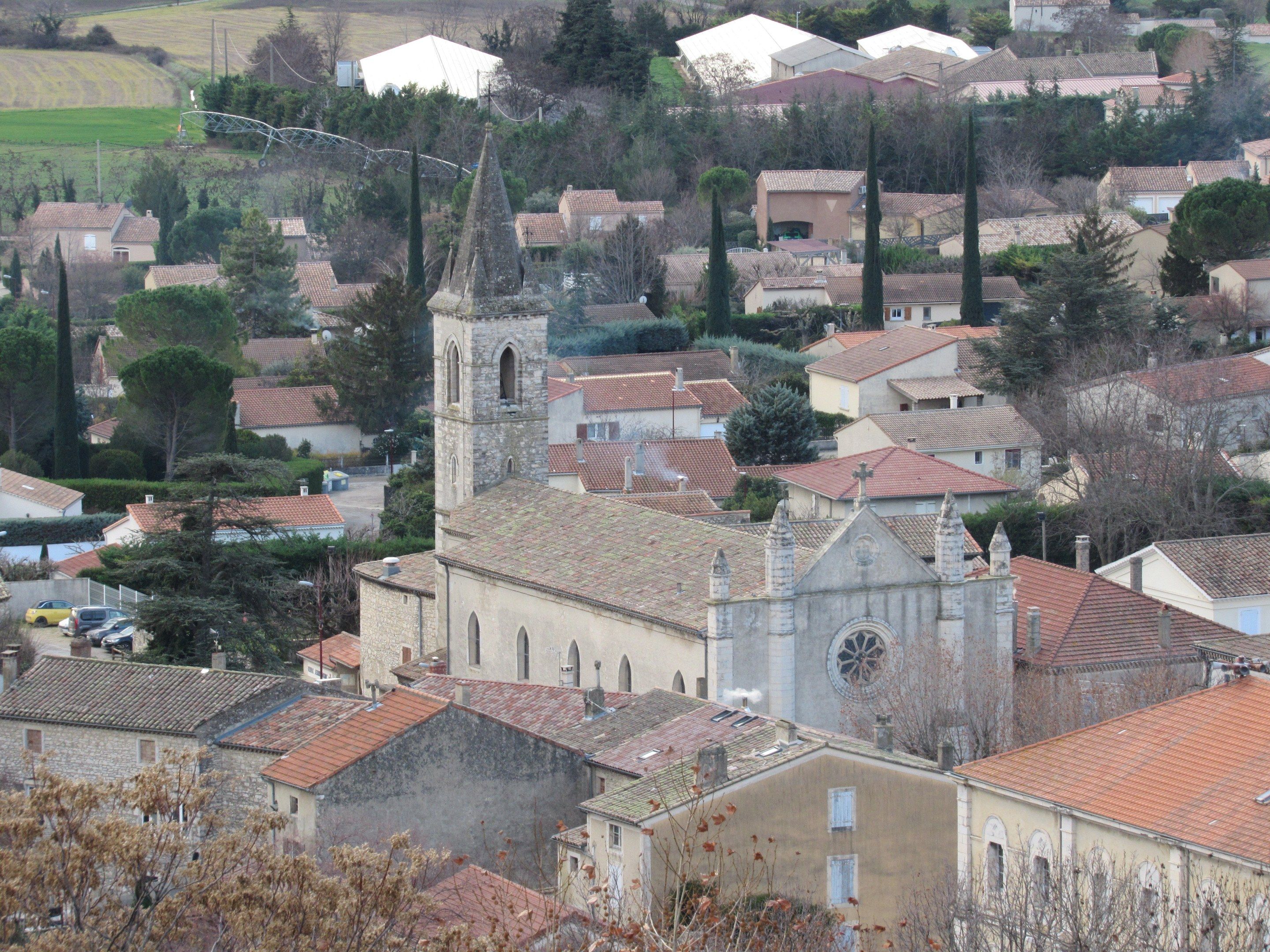 The image shows a small town with a church in the middle of it, surrounded by houses, trees, poles,...