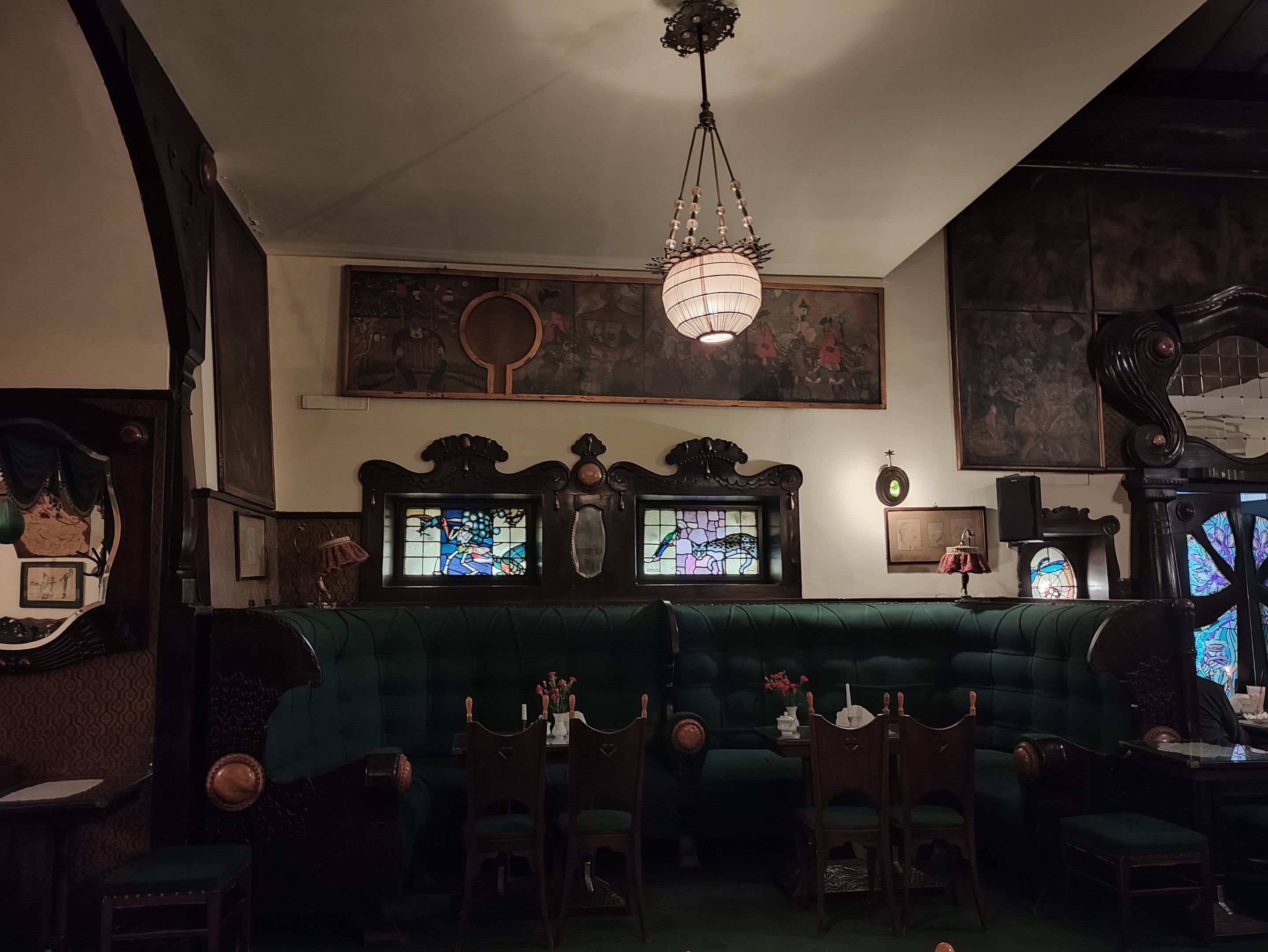 The image shows a room filled with lots of tables and chairs, flower vases on the tables, sofas, a...