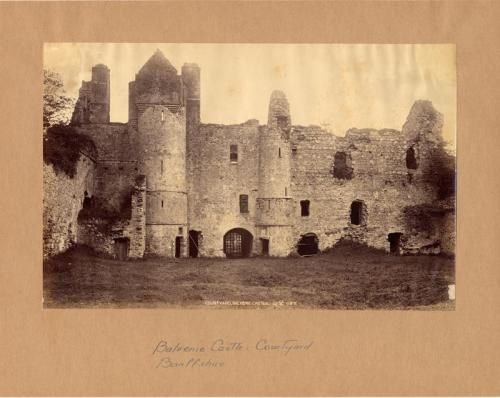 The image shows an old black and white photo of a castle in the middle of a field, surrounded by...