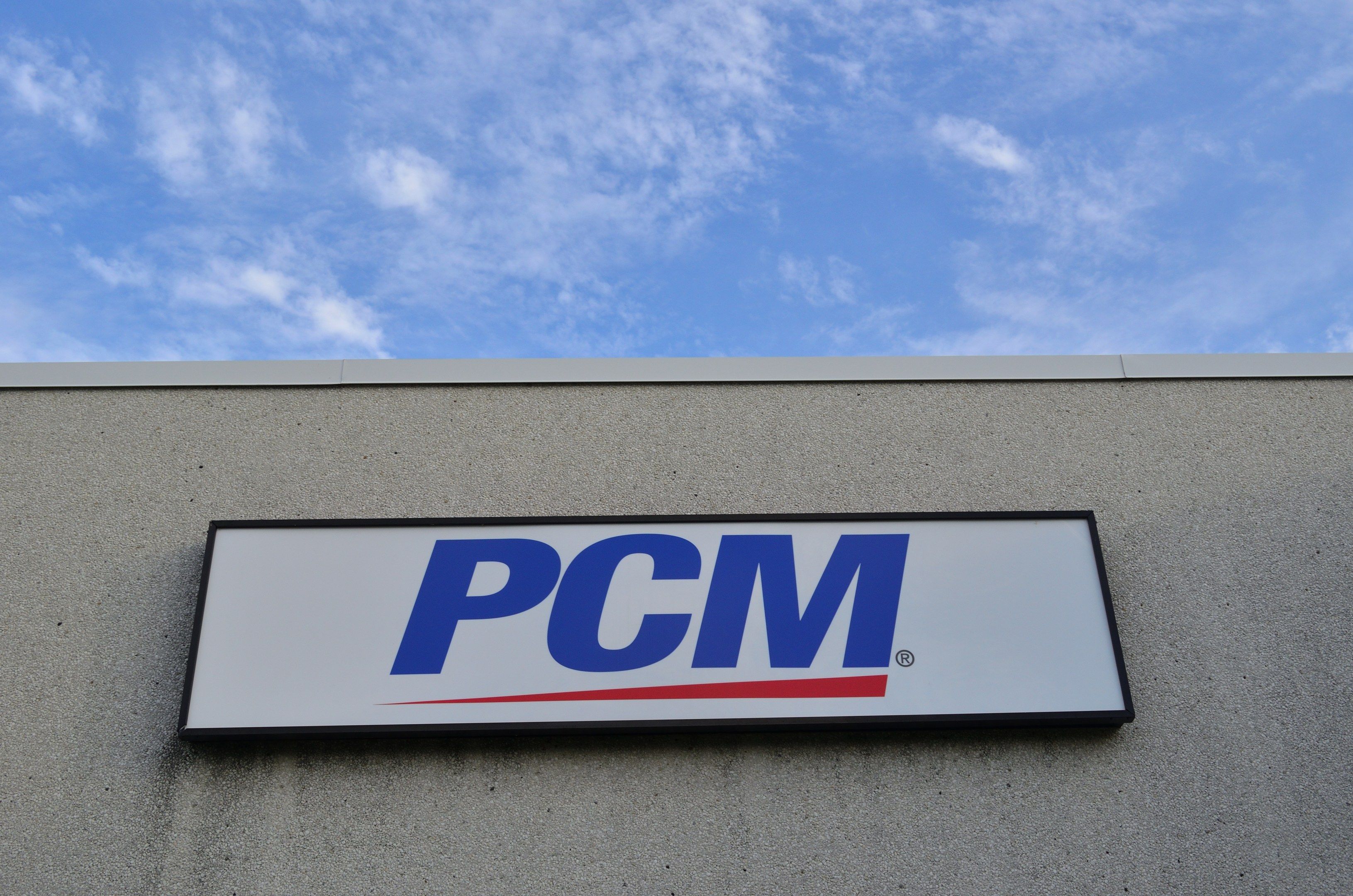 The image shows a PCM sign on the side of a building, with a board attached to the wall displaying...