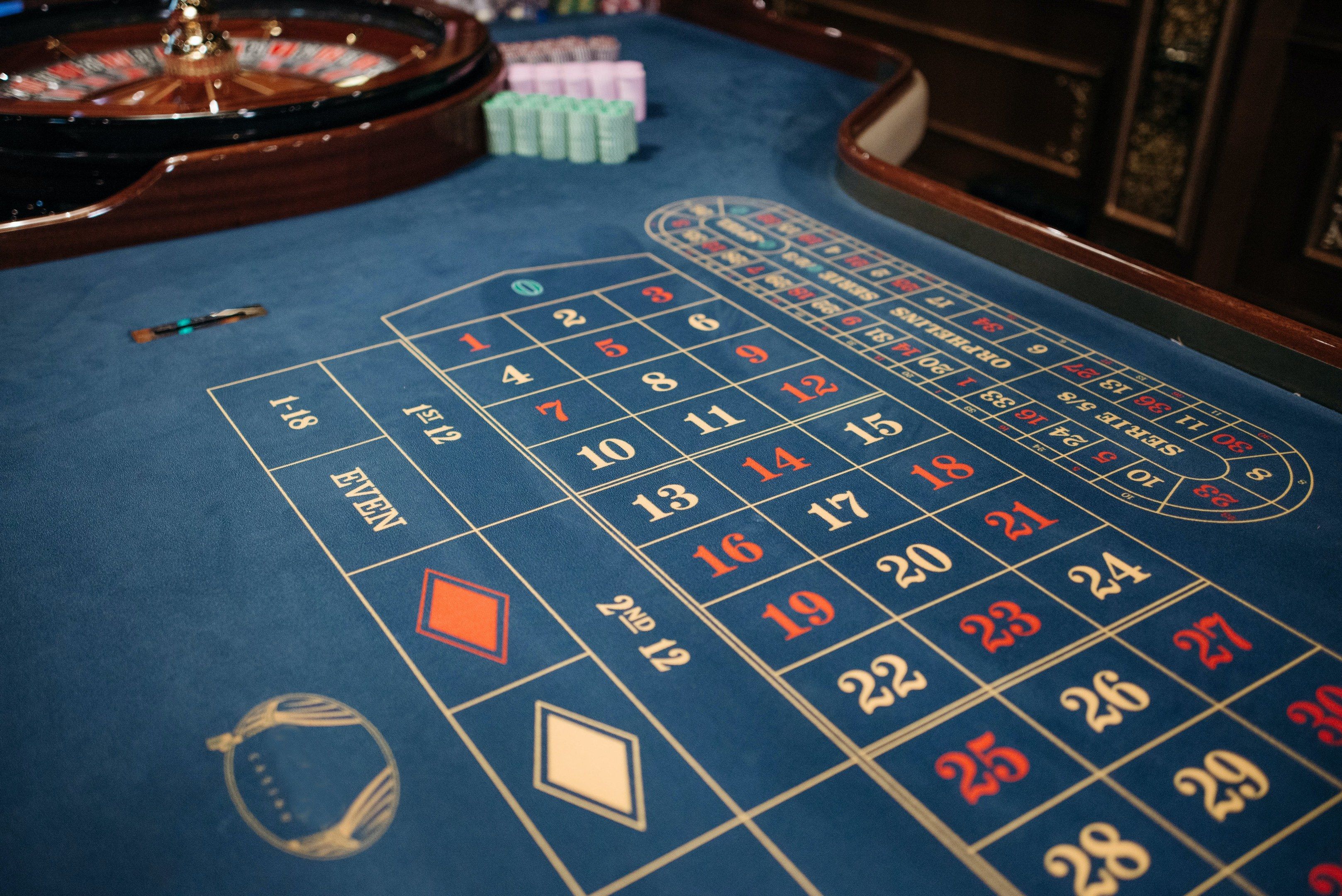 The image shows a roulette table in a casino, with a blue cloth covering the table and a spinning...