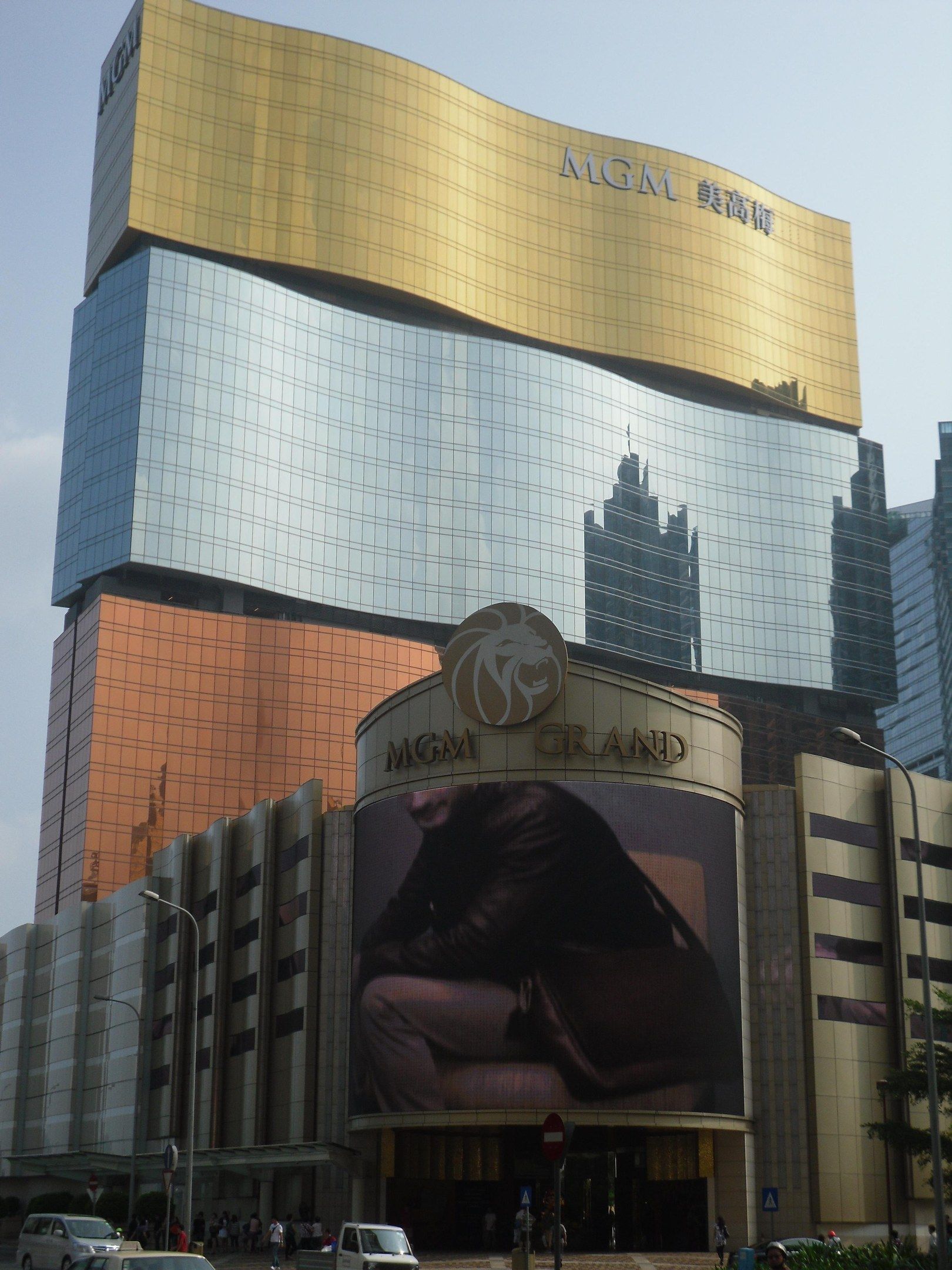 The image shows the MGM Grand Hotel and Casino in Macau, China. We can see vehicles on the road,...
