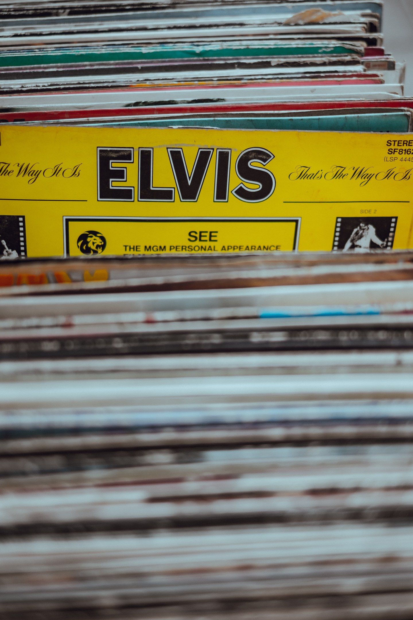 The image shows a stack of Elvis Presley records sitting on top of a table. The records are...
