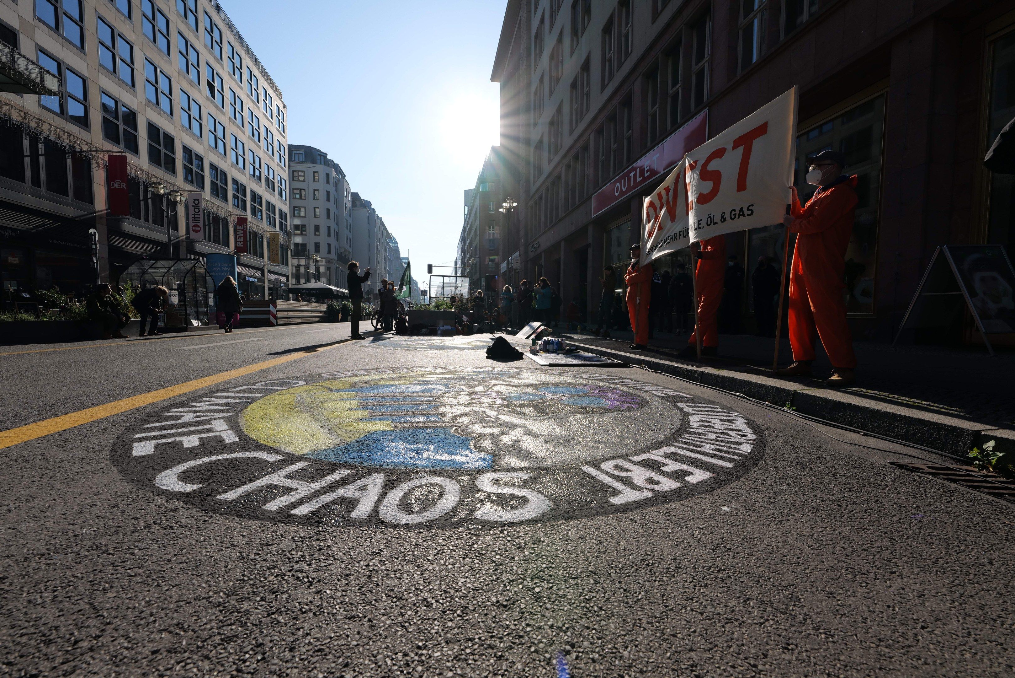 The image shows a group of people standing on the side of a street, holding banners and placards...