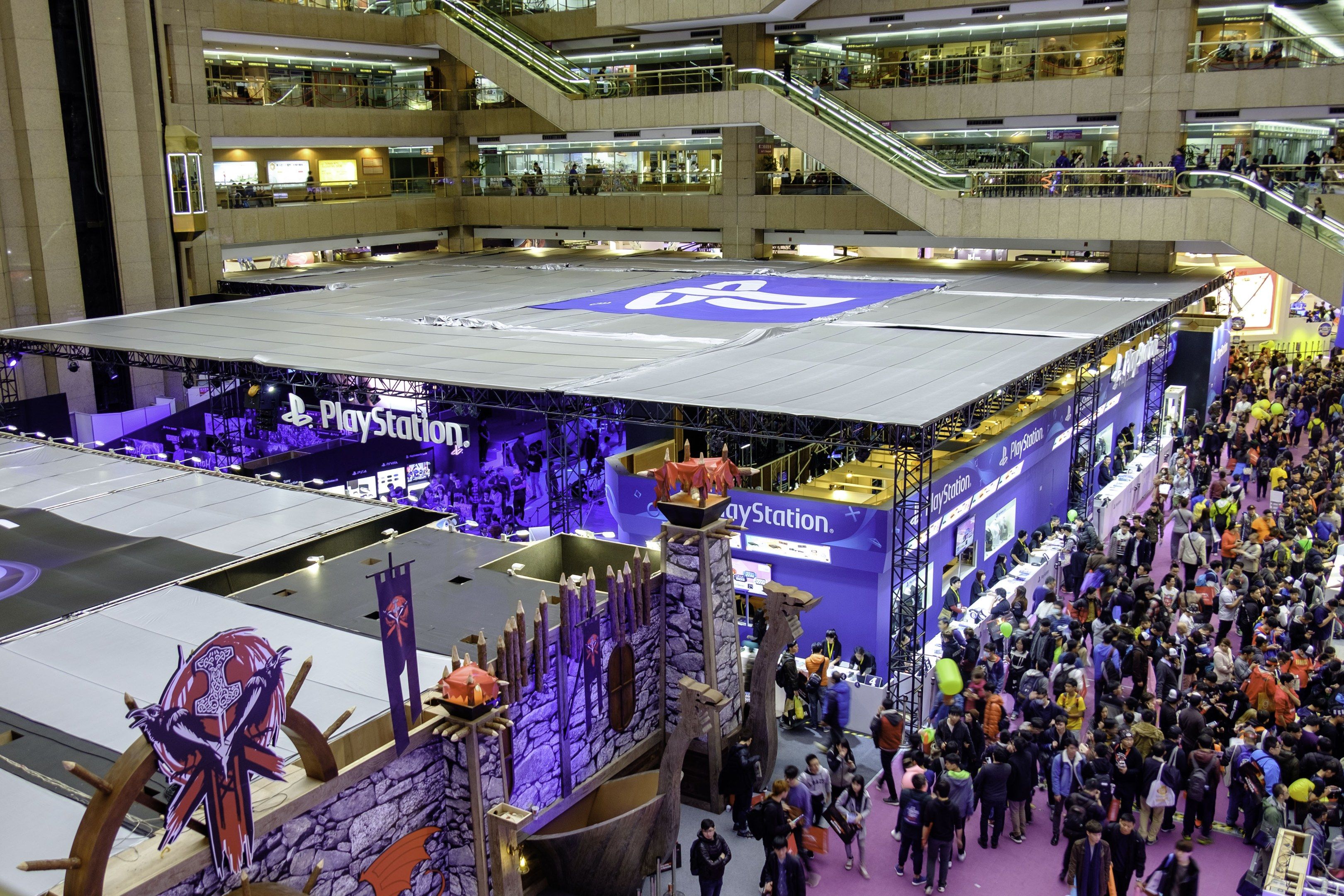 The image shows a large crowd of people standing in a large building with escalators, railings,...