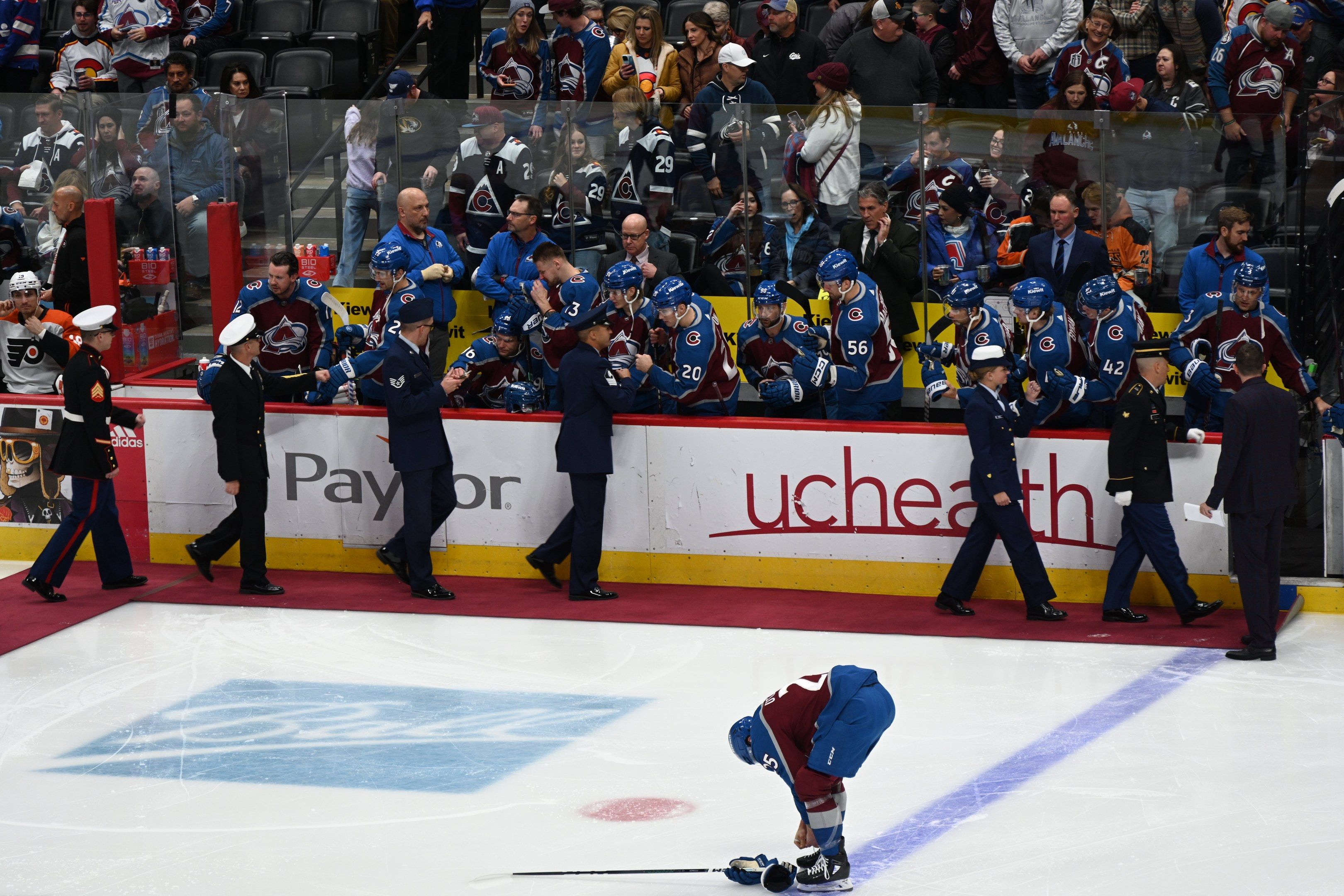 The image shows a hockey player on the ice with a stick in his hand, surrounded by a group of...
