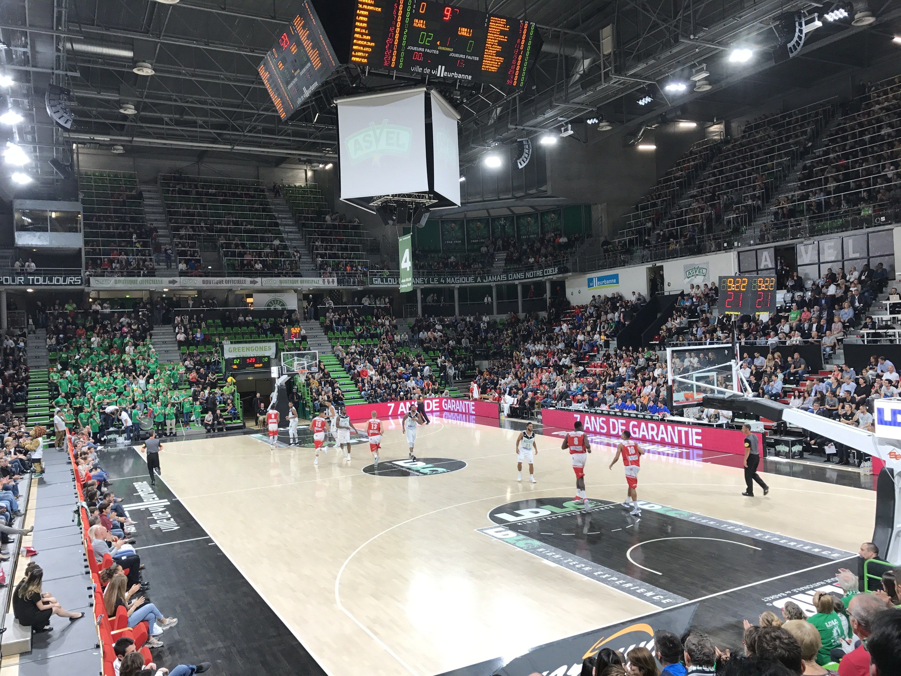 The image shows a basketball game being played in a large arena with a crowd of people watching....