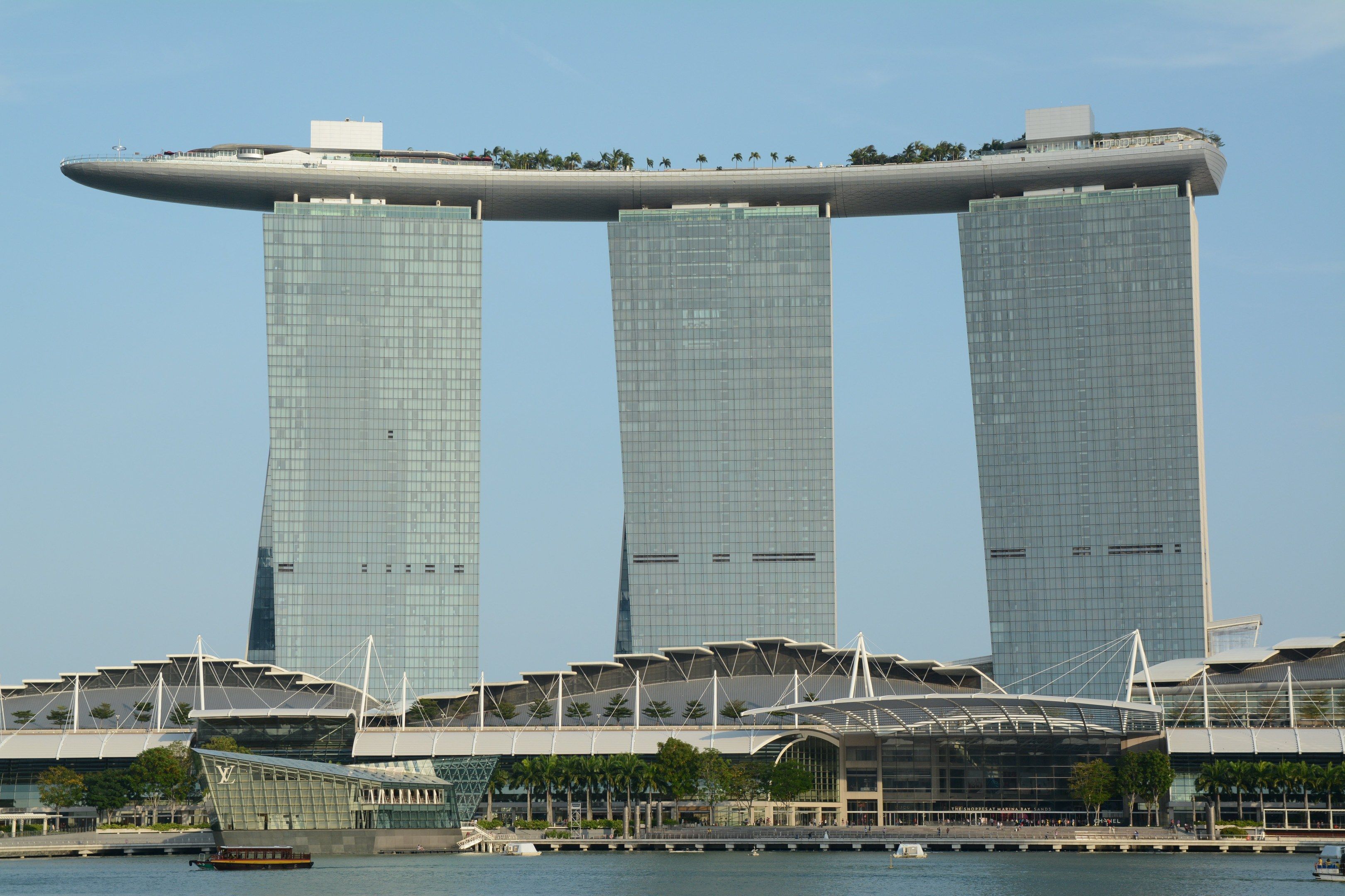 The image shows the iconic Marina Bay Sands Hotel in Singapore, with its towering skyscrapers, lush...