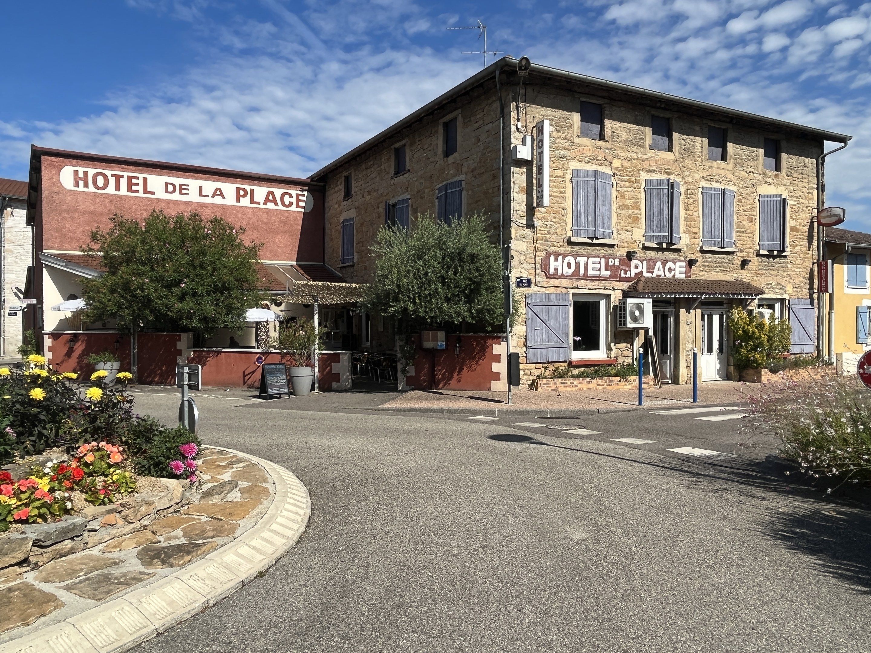 The image shows the Hotel de la Place in the village of Saint-Emilio, France. It features buildings...