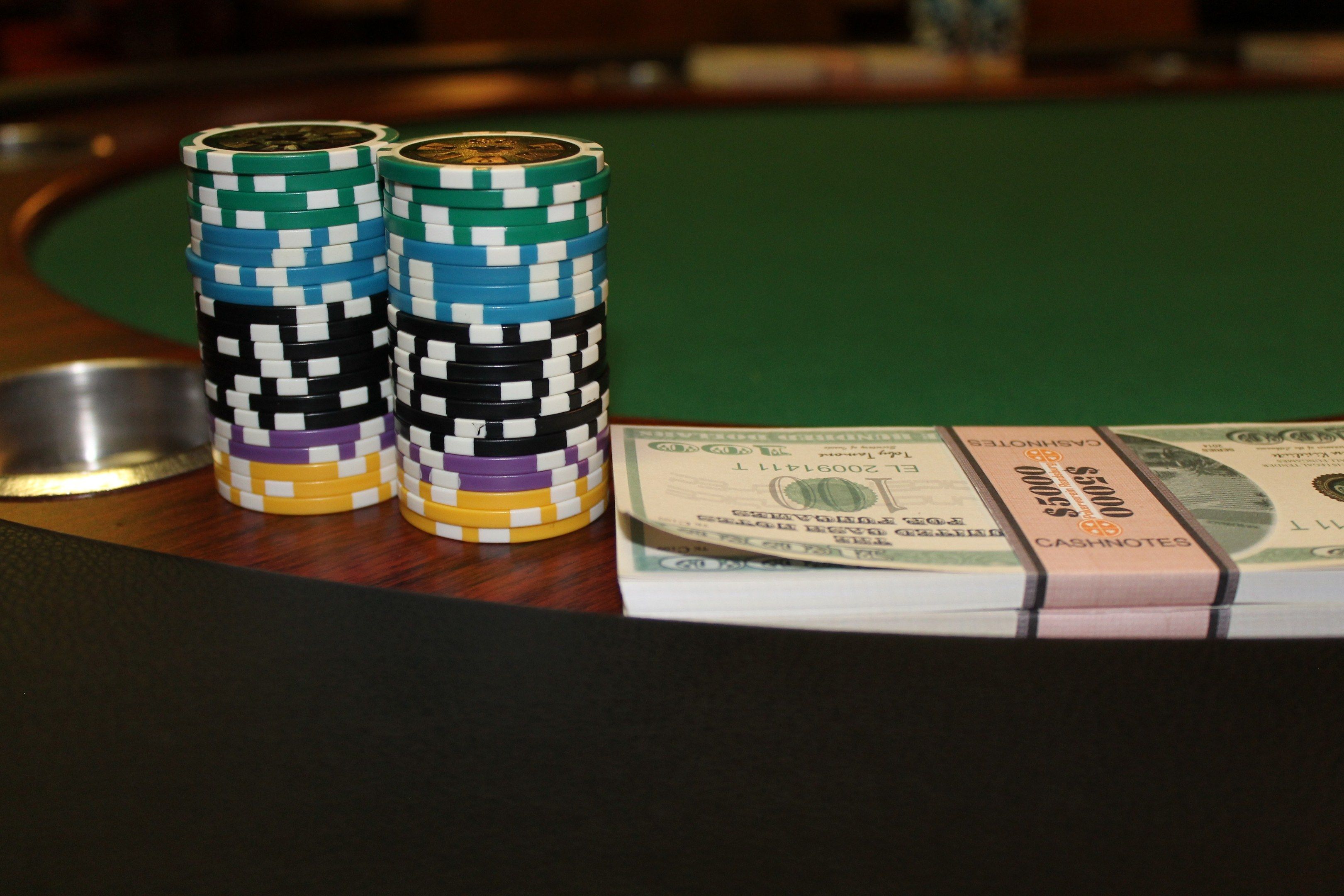 The image shows a poker table with a stack of poker chips on top of it, along with some currency...