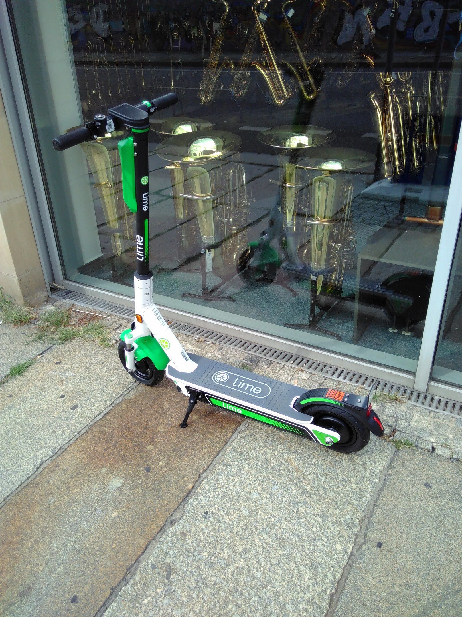 The image shows an electric scooter parked on the sidewalk in front of a store, with a glass wall...