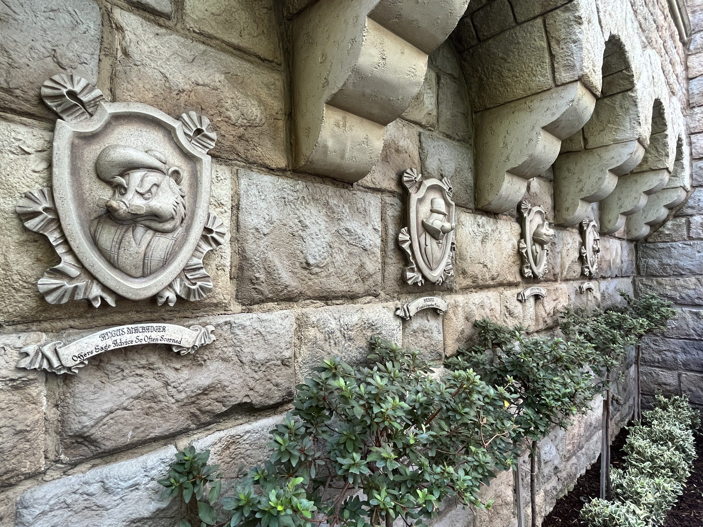 The image shows a stone building with a stone wall featuring a lion head on it, surrounded by...