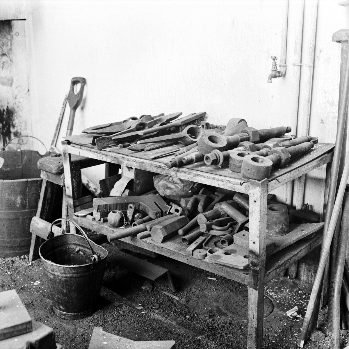 The image shows a black and white photo of a workbench with a variety of tools on it. On the left...