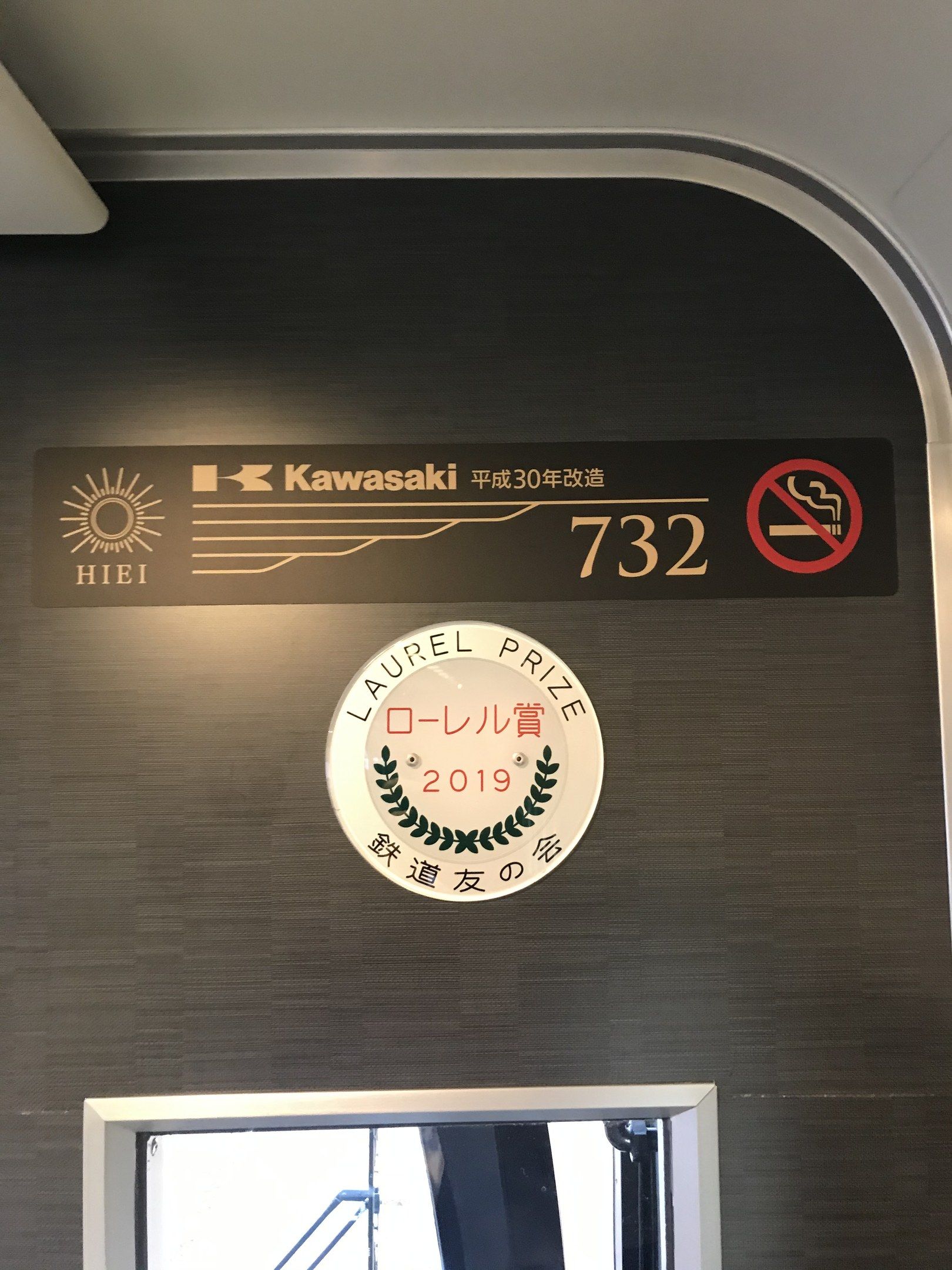 The image shows a wall with a sign on it that reads "Kawasaki 732" and a glass window on the right...