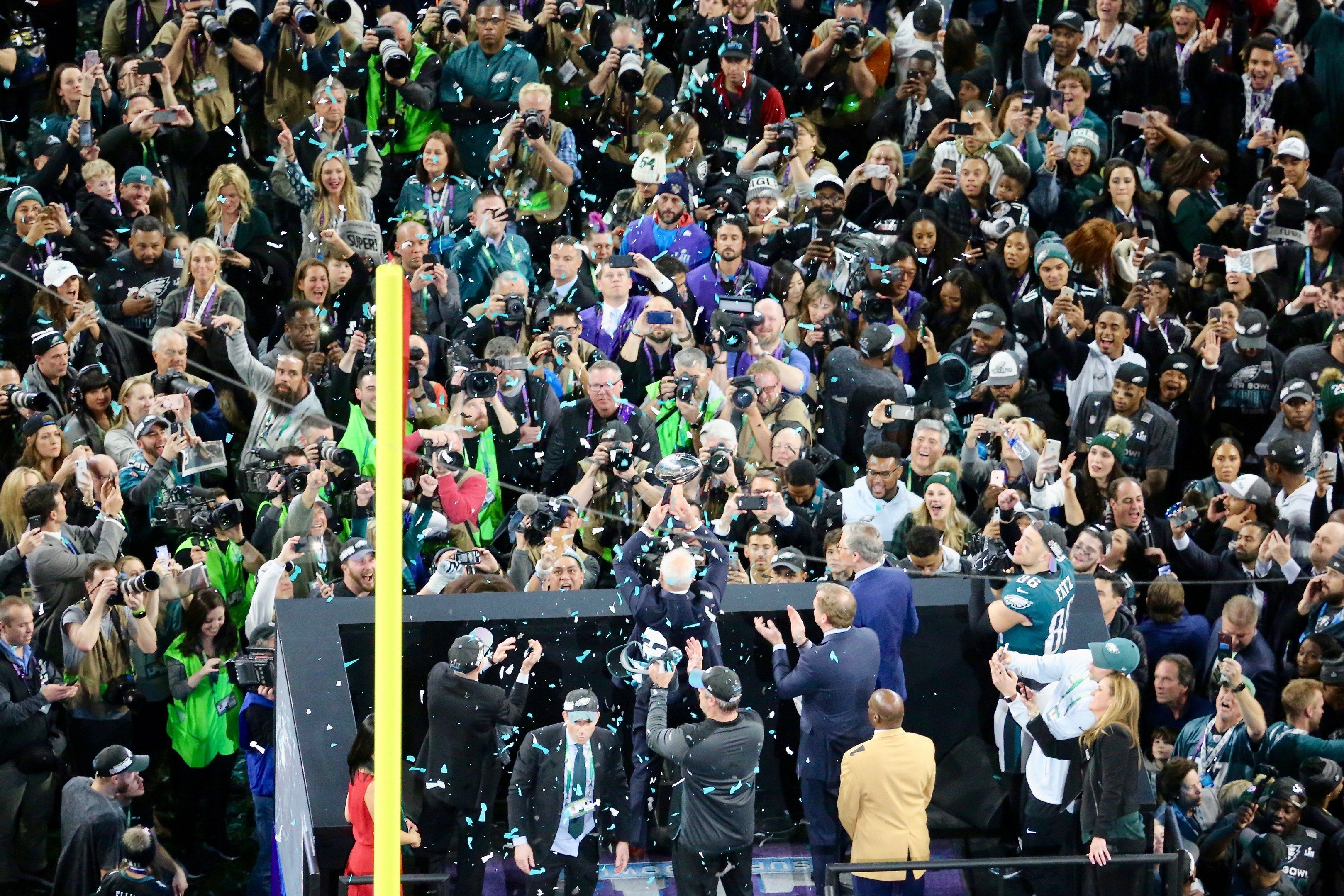 The image shows a group of people standing on top of a stage, some of them holding cameras and...