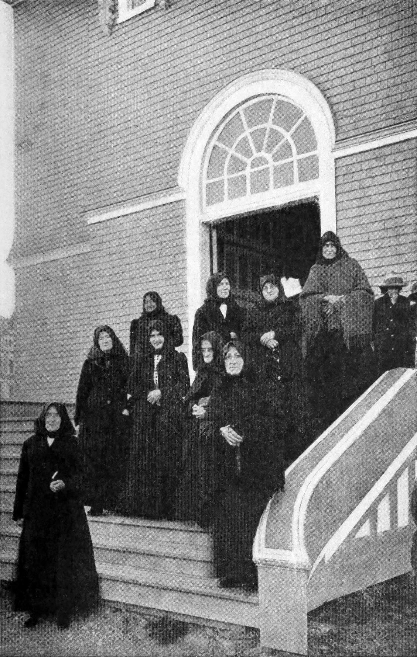 The image shows a group of women standing on the steps of a church, with a building in the...