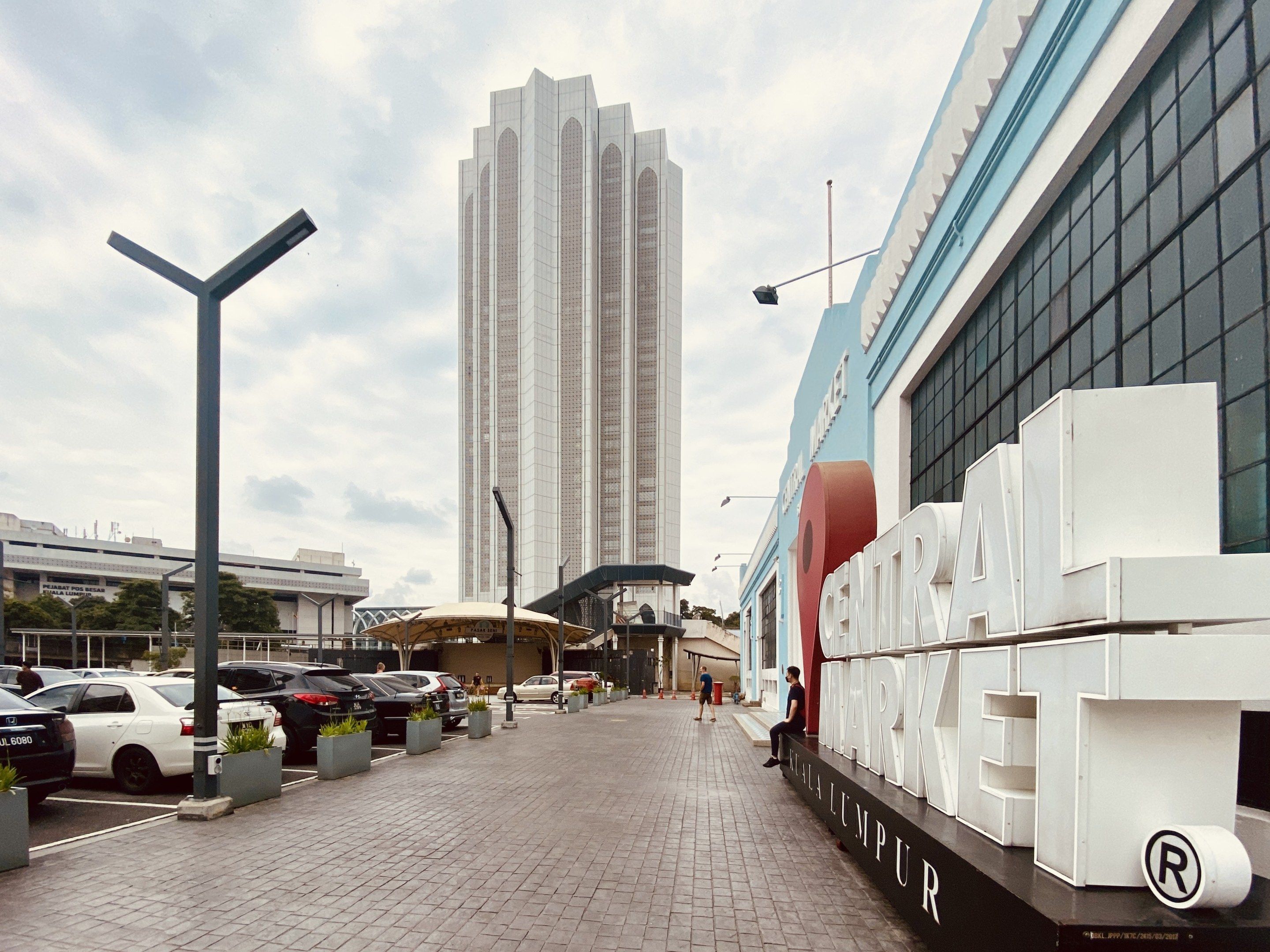 The image shows a bustling central market in Kuala Lumpur, Malaysia, with tall buildings, street...