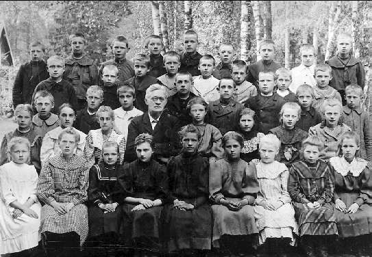 The image shows a black and white photo of a group of children posing for a picture in front of a...